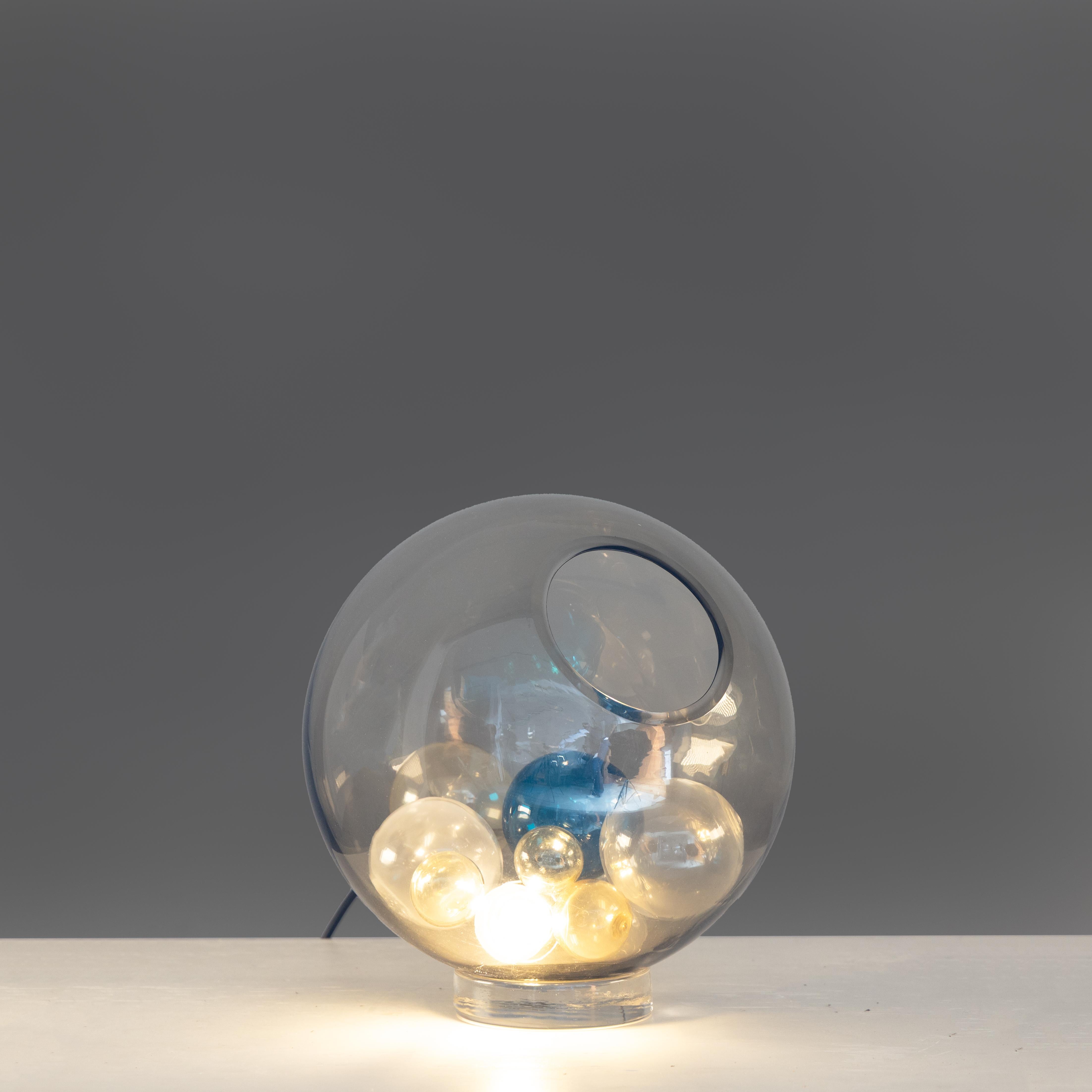 Lampada da tavolo modello “Pallotta”, progettata da Paolo Venini e Massimo Pistilli per Venini intorno al 1960. Realizzata in vetro soffiato, l’opera riflette la maestria artigianale della vetreria muranese e la capacità dei designer di coniugare