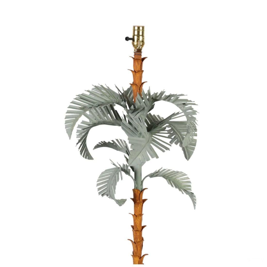 This Palm Beach Regency Style Palm Floor Lamp is a striking statement piece that brings tropical elegance to any space. Featuring a sculptural palm tree design, the lamp boasts a faux-bamboo stem adorned with layered metal palm fronds, creating a
