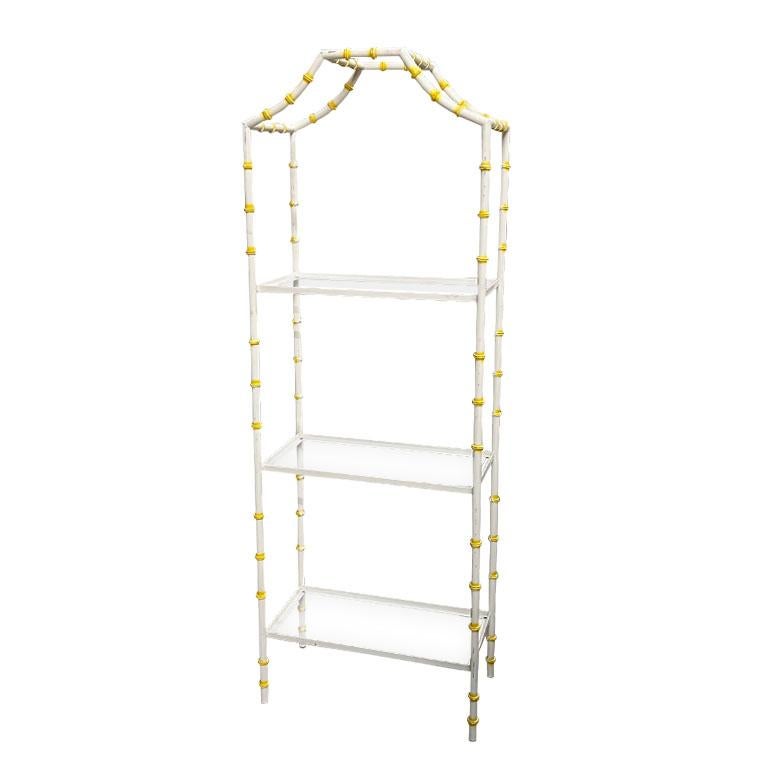 A Hollywood regency faux bamboo etagere or bookshelf. Created from metal and painted in cream and yellow, this shelf will be a great addition to any grandmillennial's home. There are three glass shelves that are newly cut and in excellent condition.