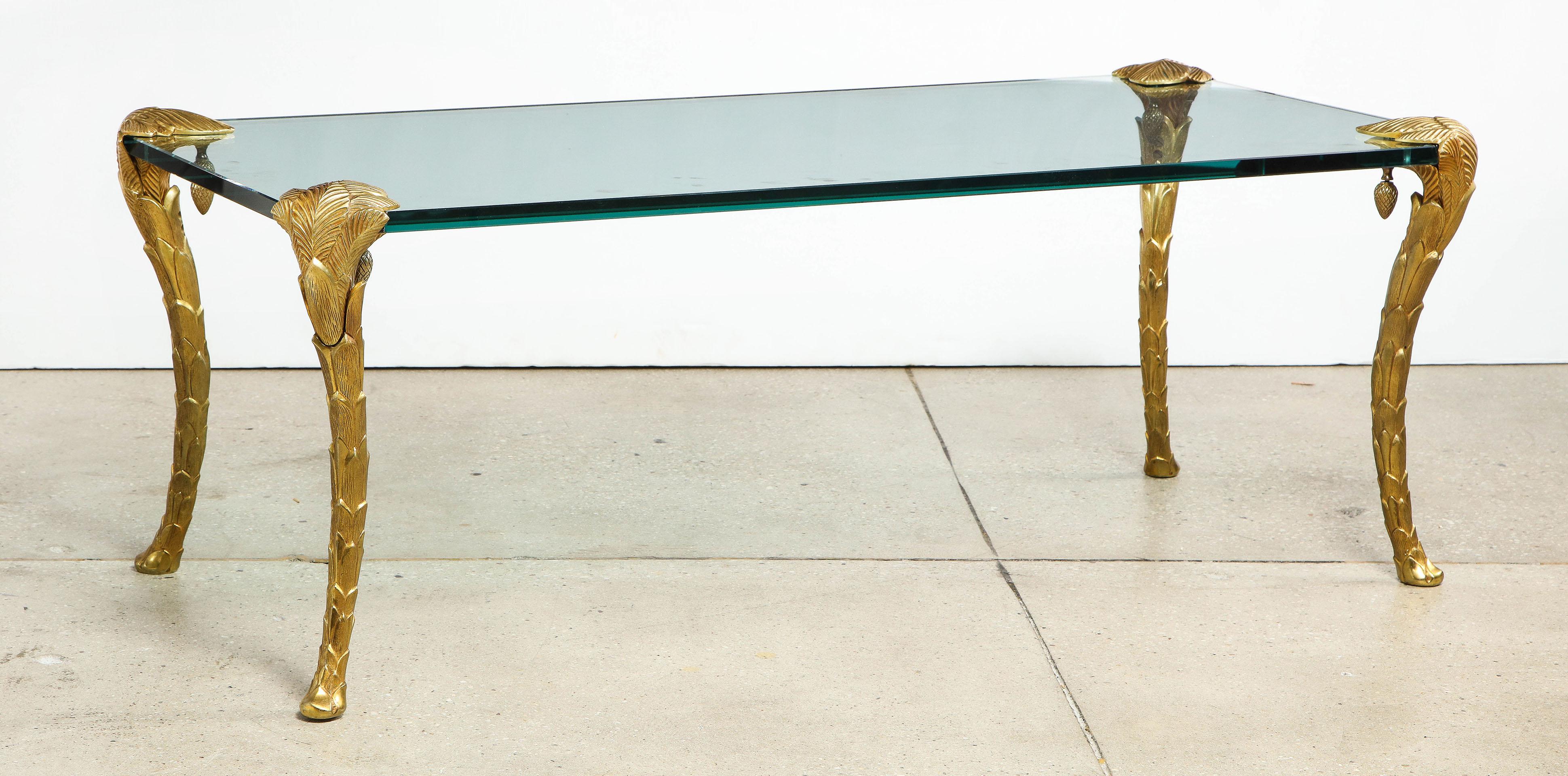 The glass top supported by four doré bronze legs in the form of palms.