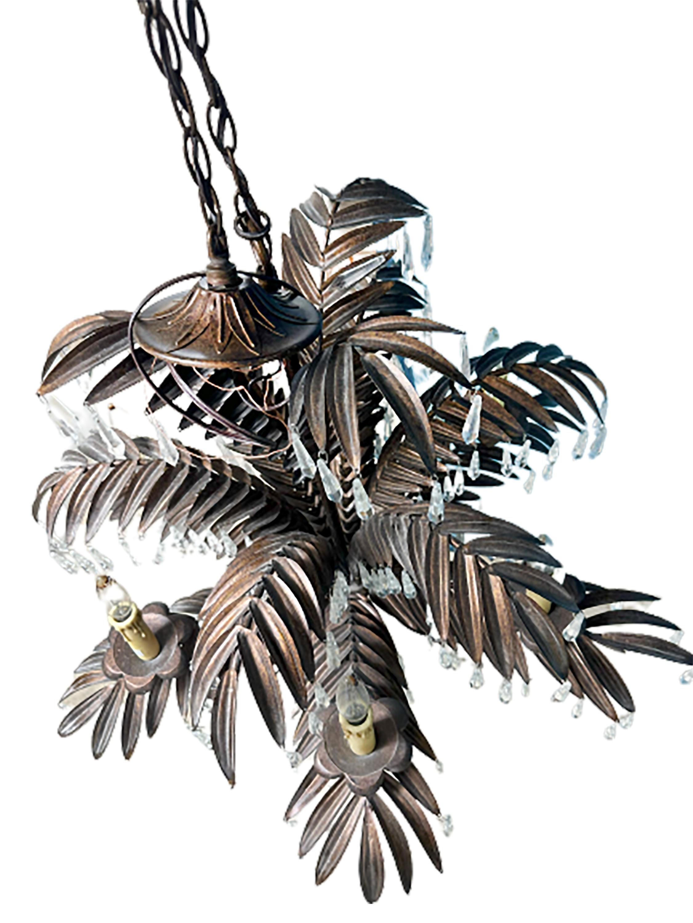 A handsome handmade palm frond chandelier. 21st century made. Iron leaf-like shapes create a lush sense of organic texture for this piece. Numerous hand cut glass crystal pieces hang down along each layer. A few faux wax candle electric lights sit