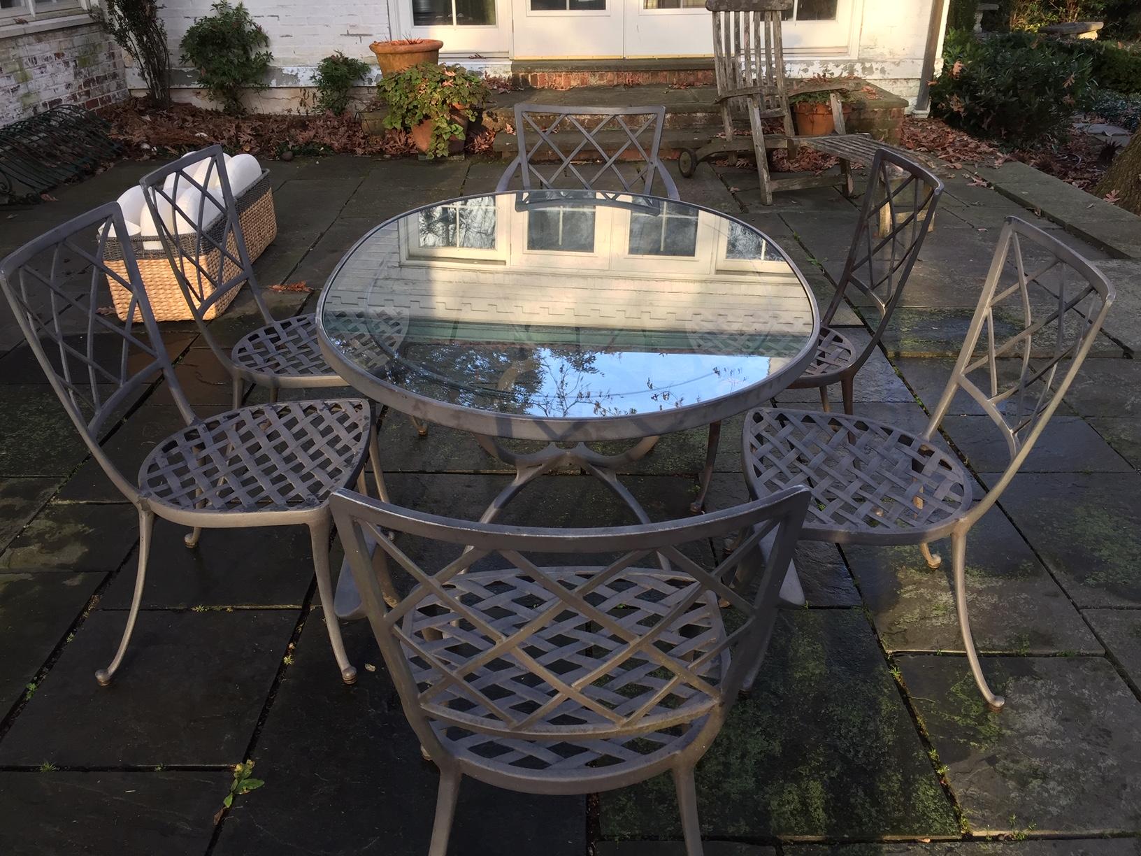 A chic outdoor metal and glass oval dining table and set of lattice back grey metal chairs, two armchairs and 4 side, having a sophisticated vibe. A rare find by Brown Jordan, circa 1960s. Custom cushions (should be cleaned or recovered) and tarp