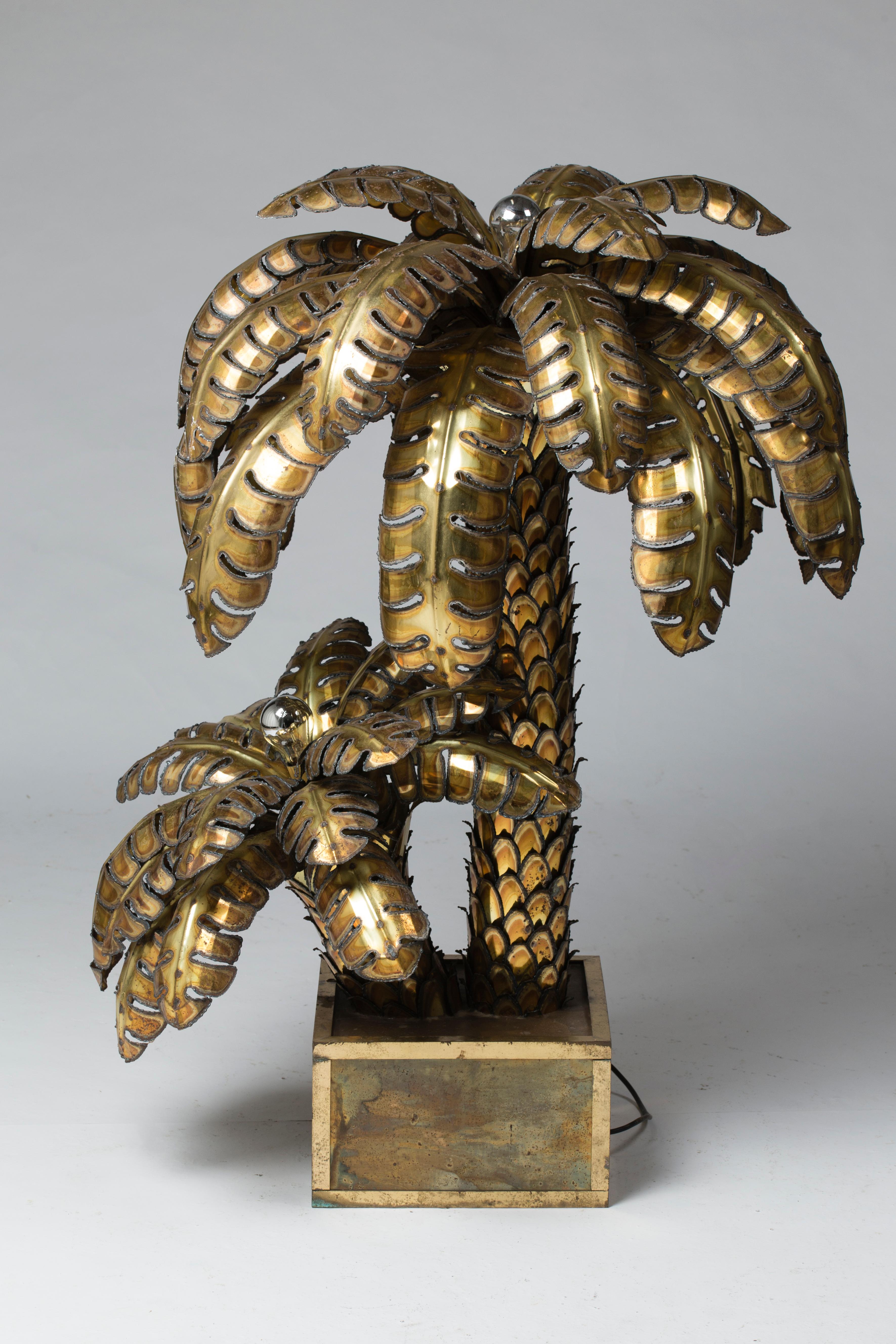 Rare palm tree table lamp with two heads, gilt and patinated iron in a square planter in oxidized brass, lined with a polished brass angle.
France, circa 1970.

Measures: Diameter 33.5 in
Height 45.3 in.