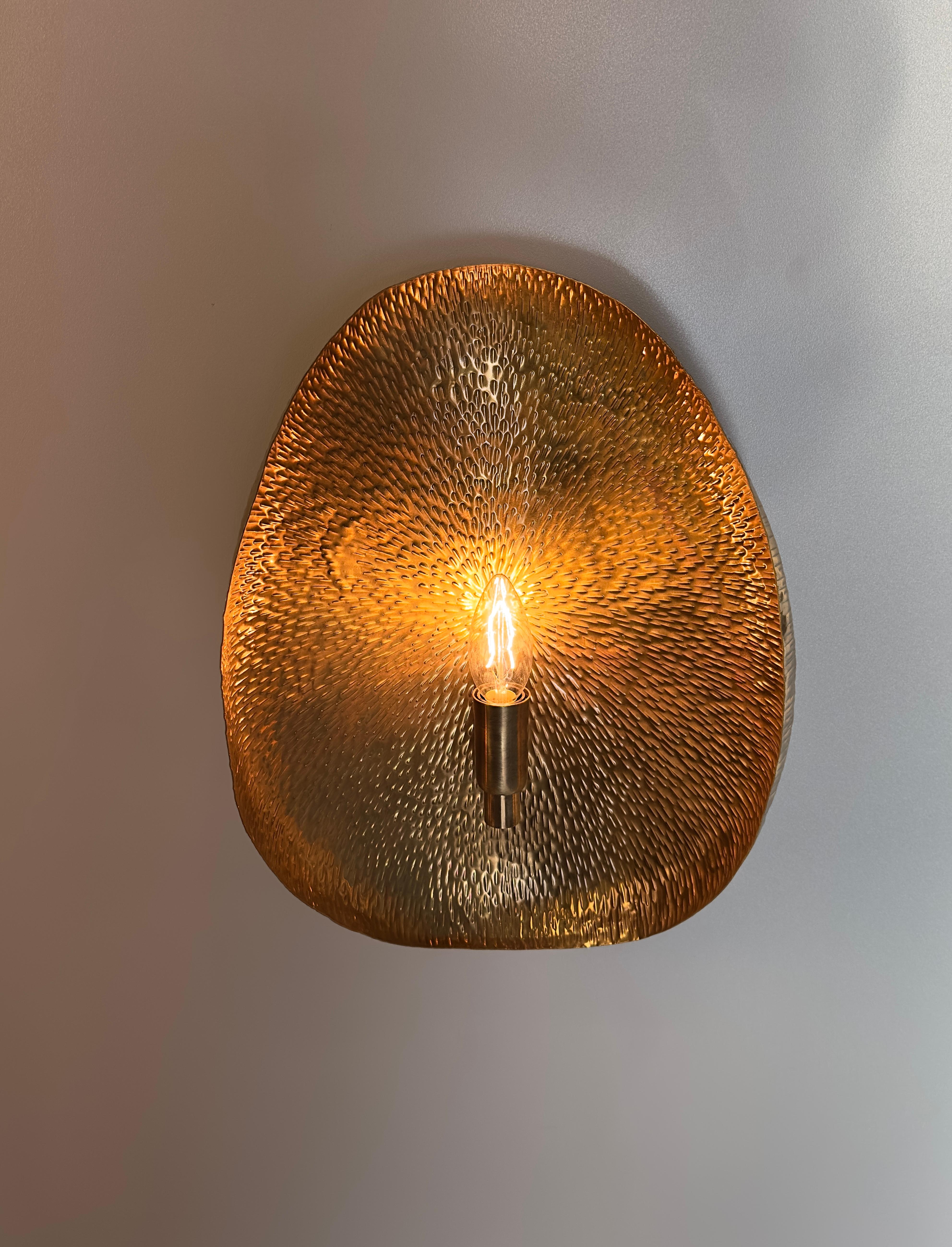 PALMA Wall Sconce, a stunning lighting fixture that is sure to add a touch of elegance and sophistication to any space. Handmade with delicate precision, this sconce is crafted from a hammered brass sheet, carefully formed into a sphere