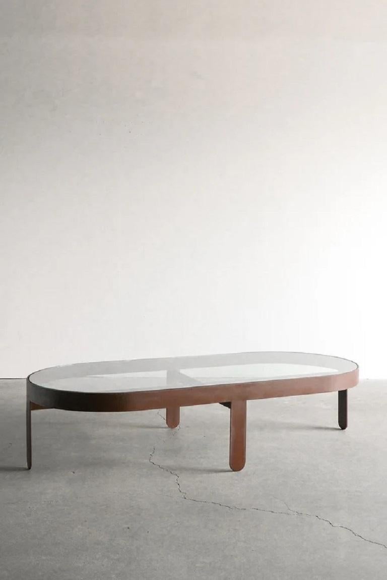 La table basse Palmas est une pièce remarquable qui allie harmonieusement forme et fonction. Le plateau en verre, enchâssé dans un épais bandeau et des pieds, confère à la table un aspect épuré et contemporain. Les pieds en sangle, arrondis en bas,