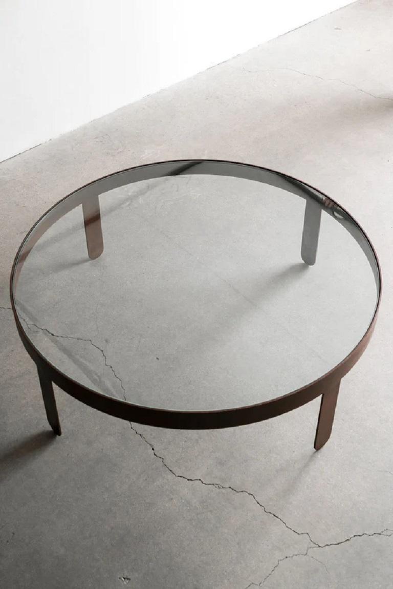 The Palmas Coffee Table is a striking piece that seamlessly blends form and function. The glass top, encased in a thick banded strip and legs, gives the table a sleek and contemporary feel. The strap legs, rounded at the bottom, soften the edges and