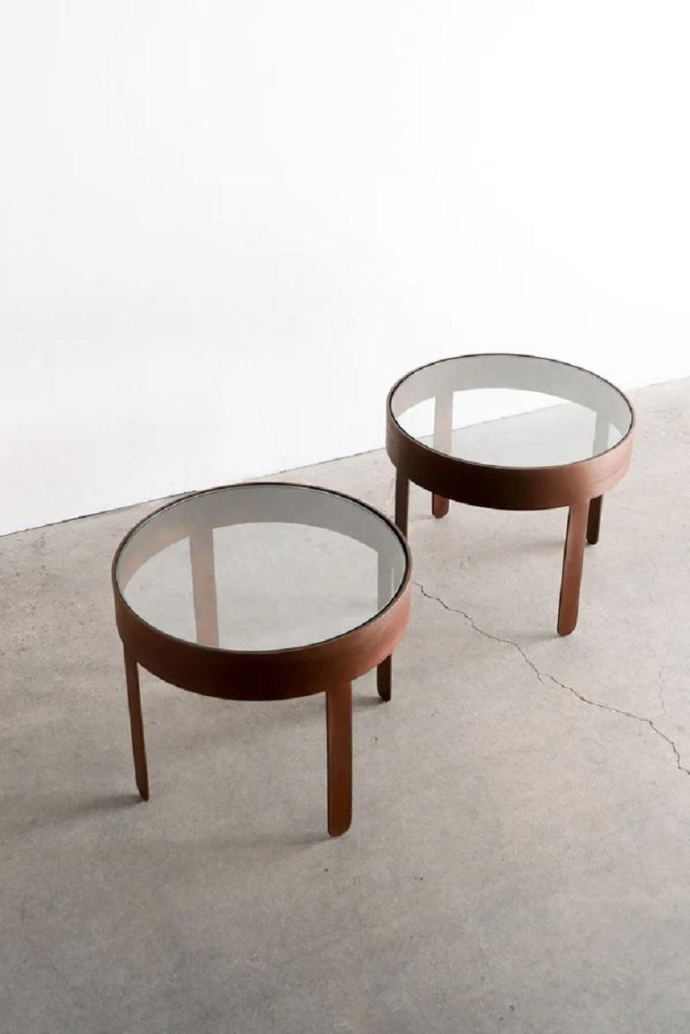 La table d'appoint Palmas est un complément rustique, inspiré du désert, à un espace de vie. Le plateau rond en verre est entouré d'une bande épaisse et soutenu par des pieds en sangle qui adoucissent les bords de la pièce. Les pieds sont arrondis