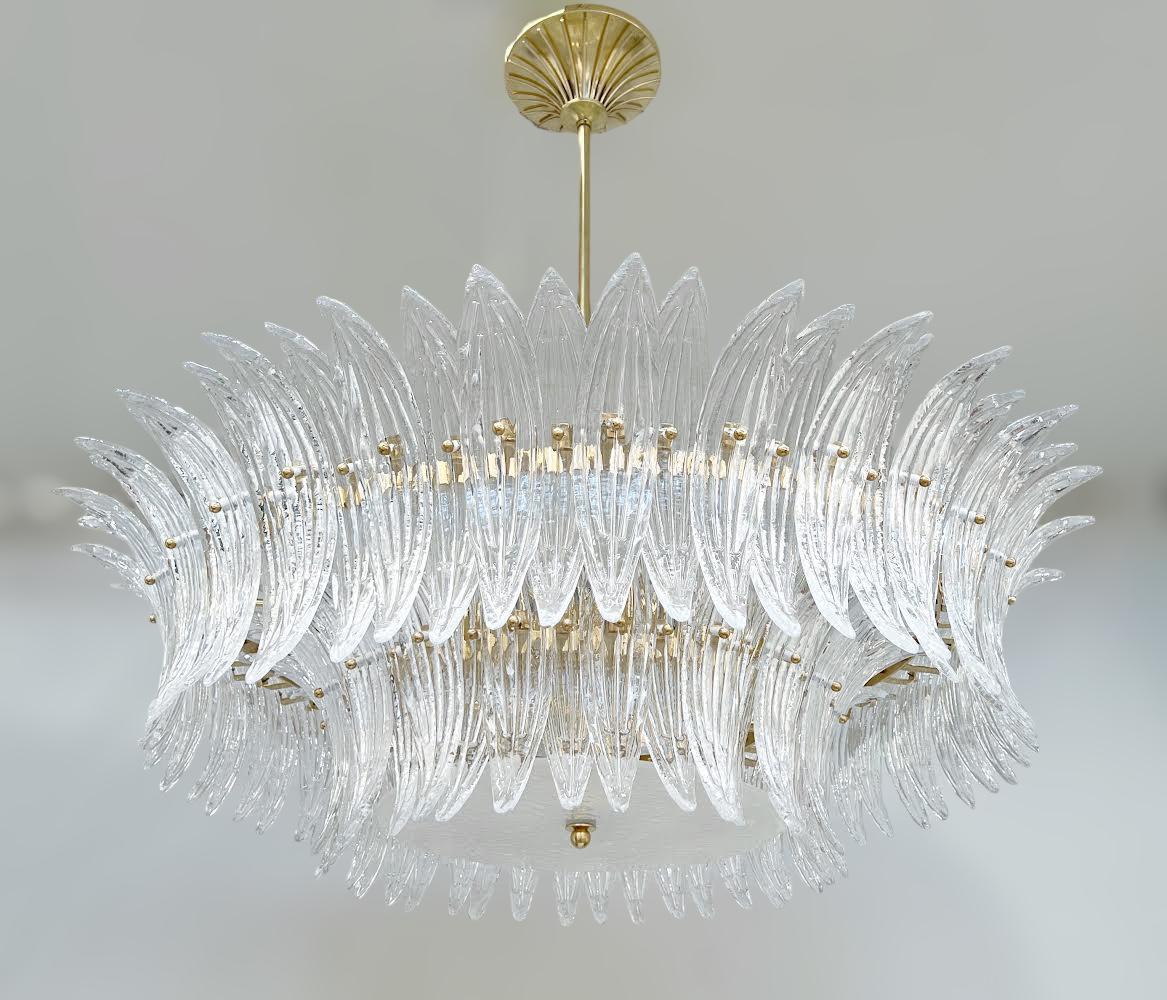 Lampadario italiano Palmette con foglie in vetro di Murano trasparente montate su una struttura in ottone naturale non laccato con un diffusore in vetro di Murano sabbiato e testurizzato / Made in Italy
Diametro di 39,5 pollici, altezza di 13