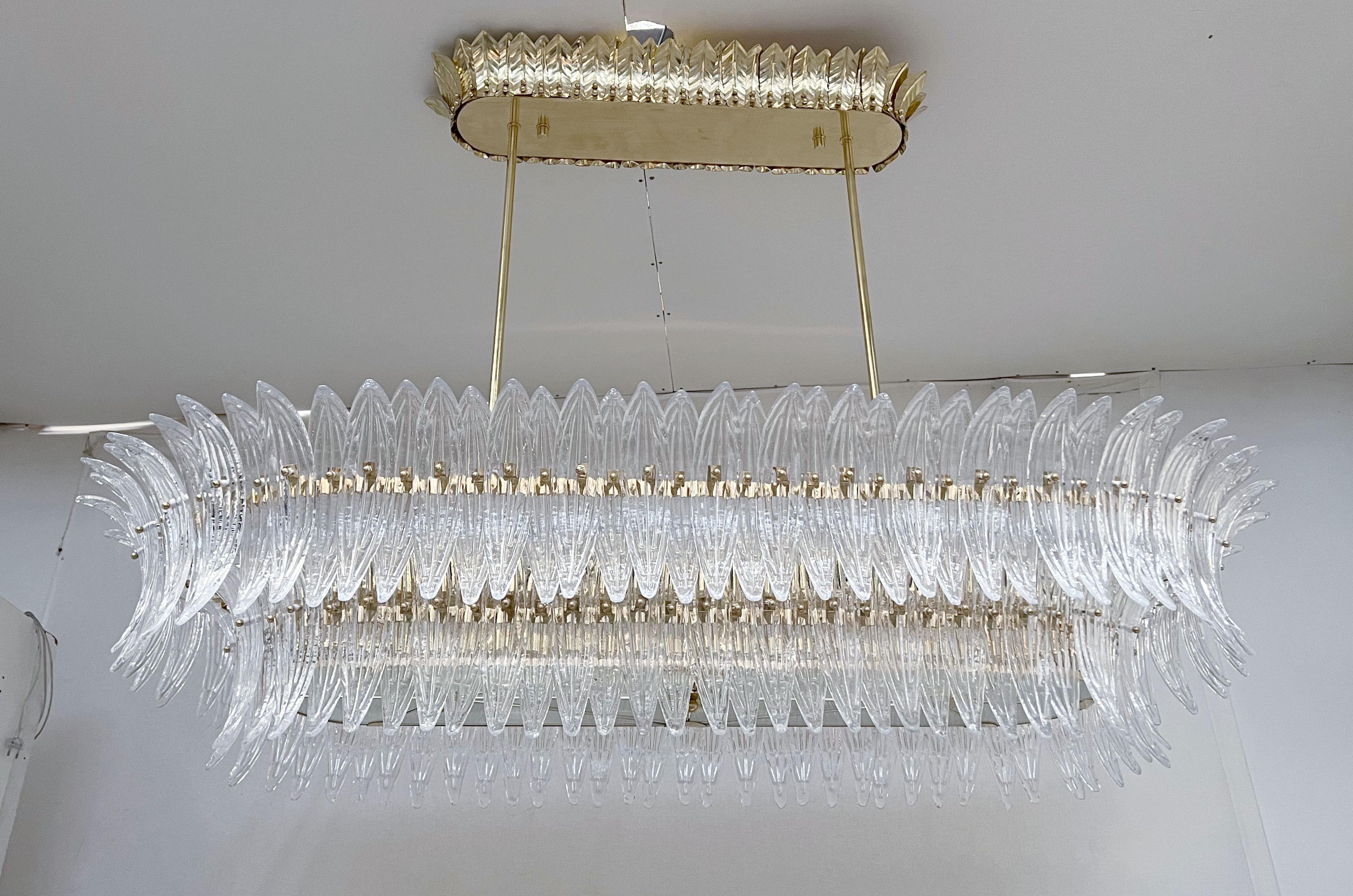 Italian Palmette chandelier shown in clear Murano glass leaves mounted on unlacquered natural brass finish frame with frosted bottom glass diffusers / Made in Italy
Length 66 inches, width 31.5 inches, height 13 inches, total height 48 inches