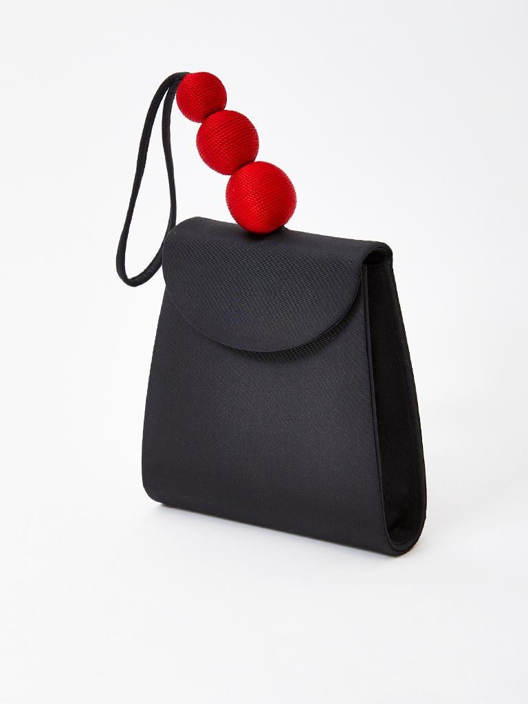 Paloma Picasso, black textured silk, structured, wristlet, evening bag having a flap closure with a hidden snap and three red, silk decorative, spheres detail  as part of the handle. 