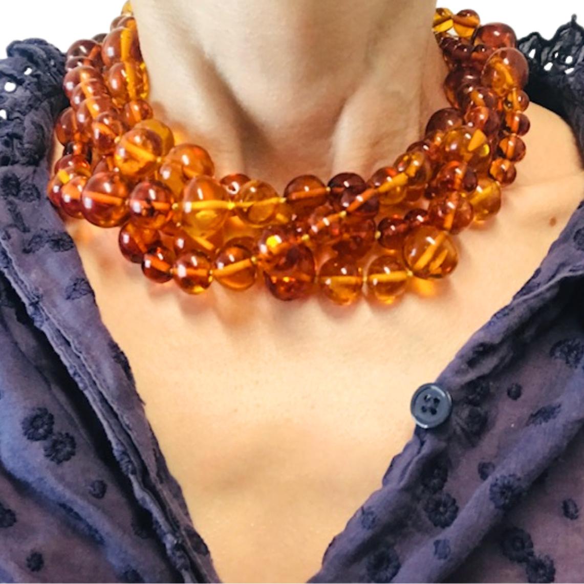This vintage necklace consists of multiple strands of polished amber beads in warm honey and cognac tones. The beads vary in size, with the smallest ones placed near the clasp and the largest positioned toward the front, creating a natural graduated