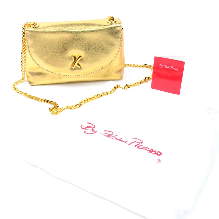 This is a beautiful gold leather Paloma Picasso vintage crossbody handbag with gold tone chain shoulder strap hardware. This little structured handbag has a flat base and a flap opening with metal snap closure. The front of the handbag has the