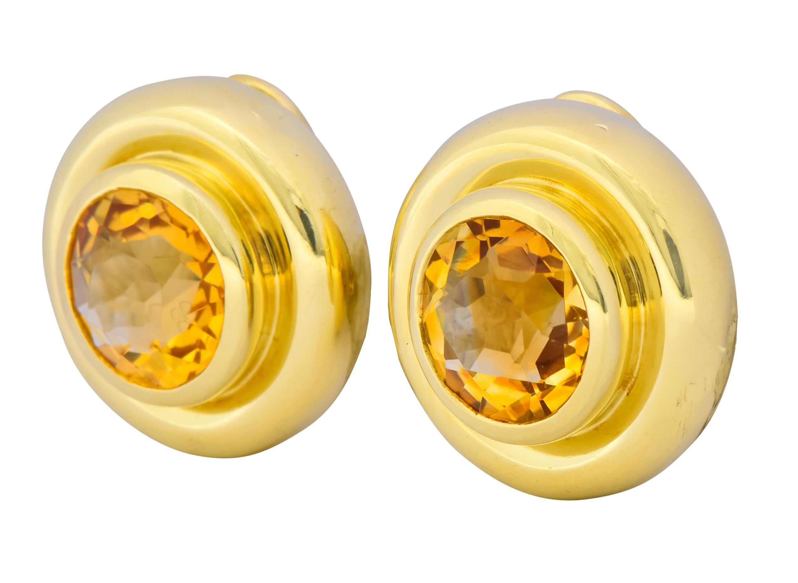 Each earring centers a round mixed cut citrine measuring approximately 10.4 mm, transparent and a warm orangey-yellow

Bezel set in a polished gold circular surround

Completed by hinged omega backs and posts

Fully signed Tiffany & Co. Paloma