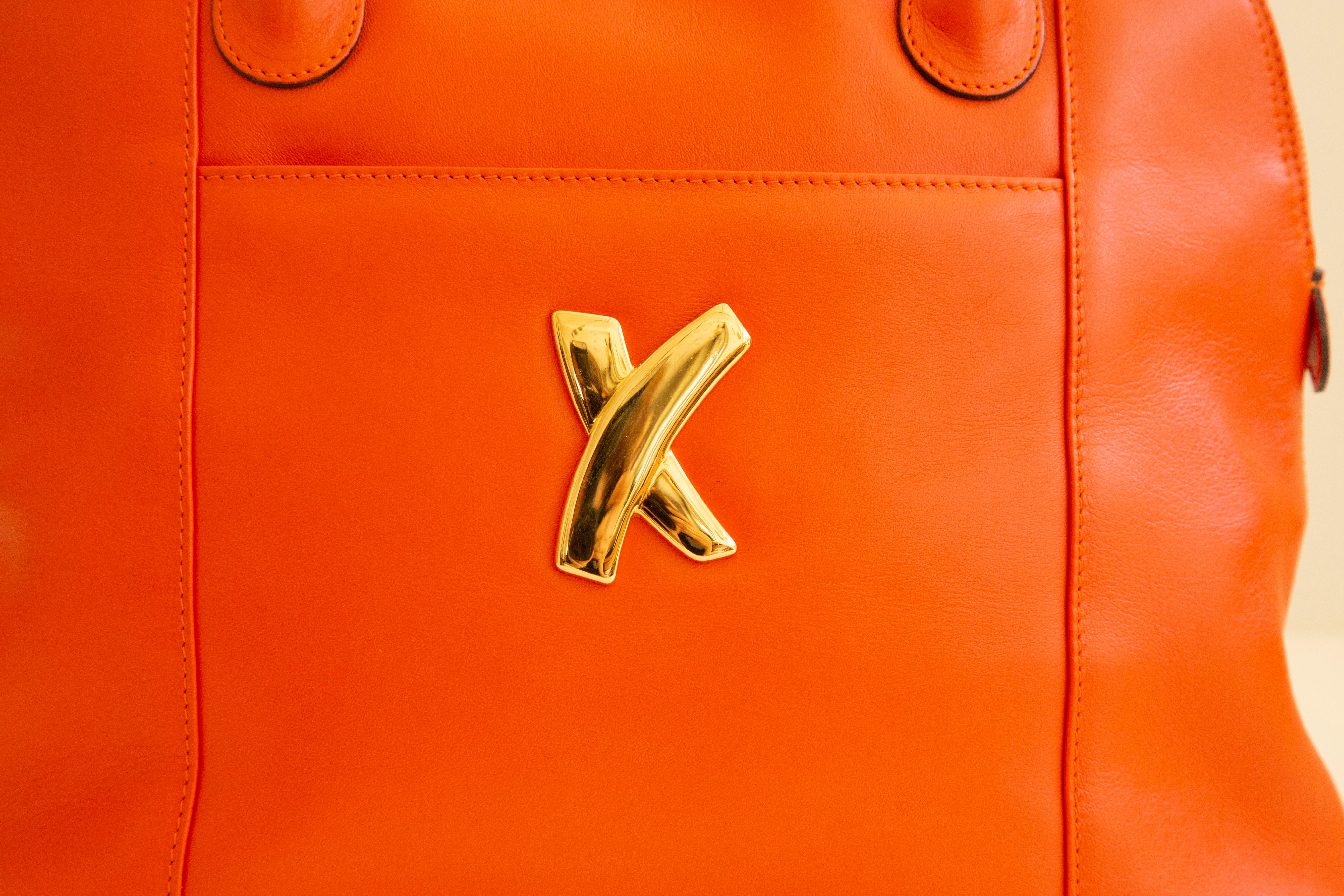 A vintage top handle bag designed by Paloma Picasso in the 1980s-90s. The bag is crafted of smooth bright soft orange leather, and it featured gold tone hardware. The interior is lined with the Paloma Picasso logo light beige fabric, and next to the