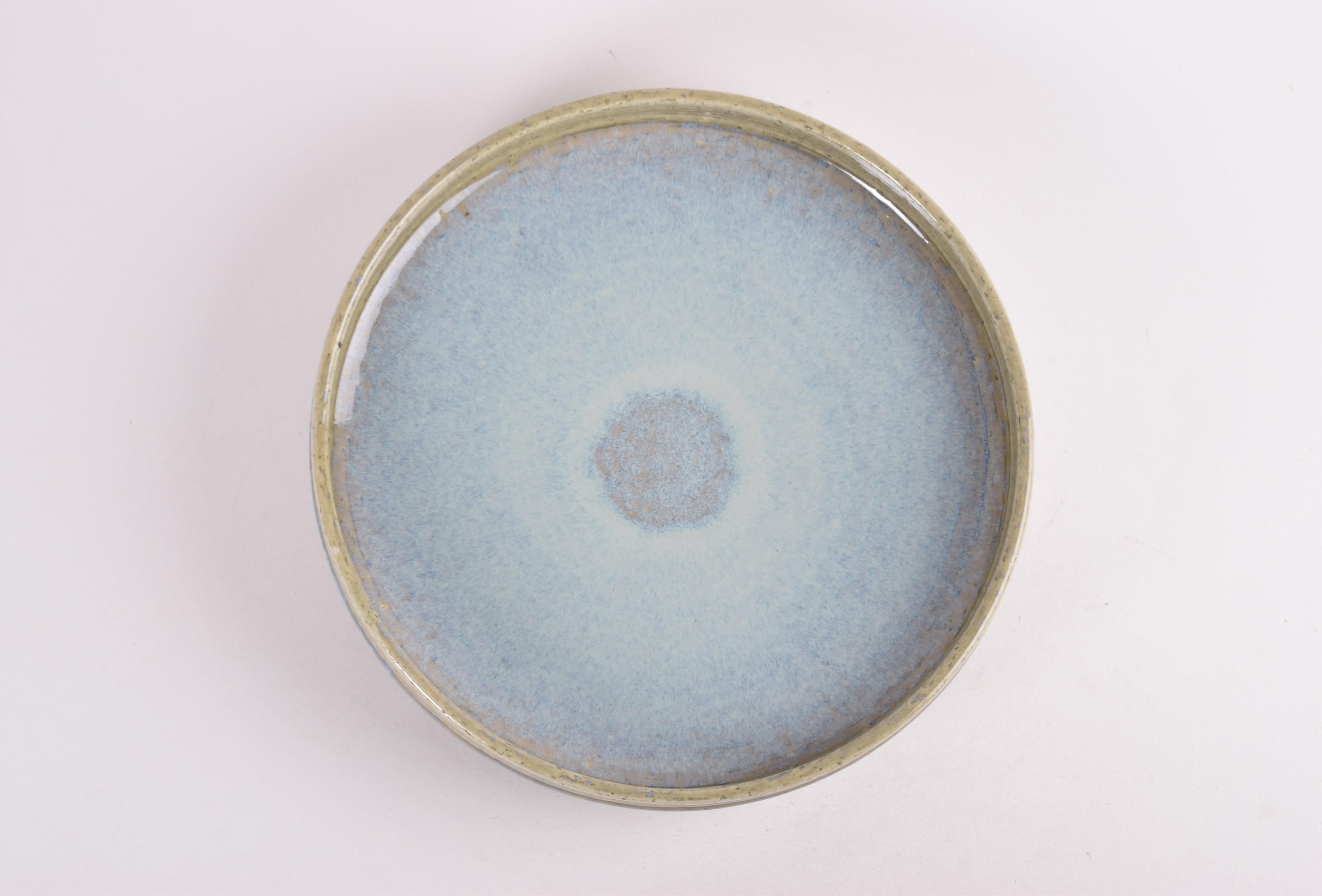 A large ceramic charger by Per Linnemann-Schmidt for Palshus Denmark. Made in the 1960s.
It is made with chamotte clay which gives a rough and vivid surface. The glaze is pale blue in center turning into green. On outside a blue ribbon contrasts