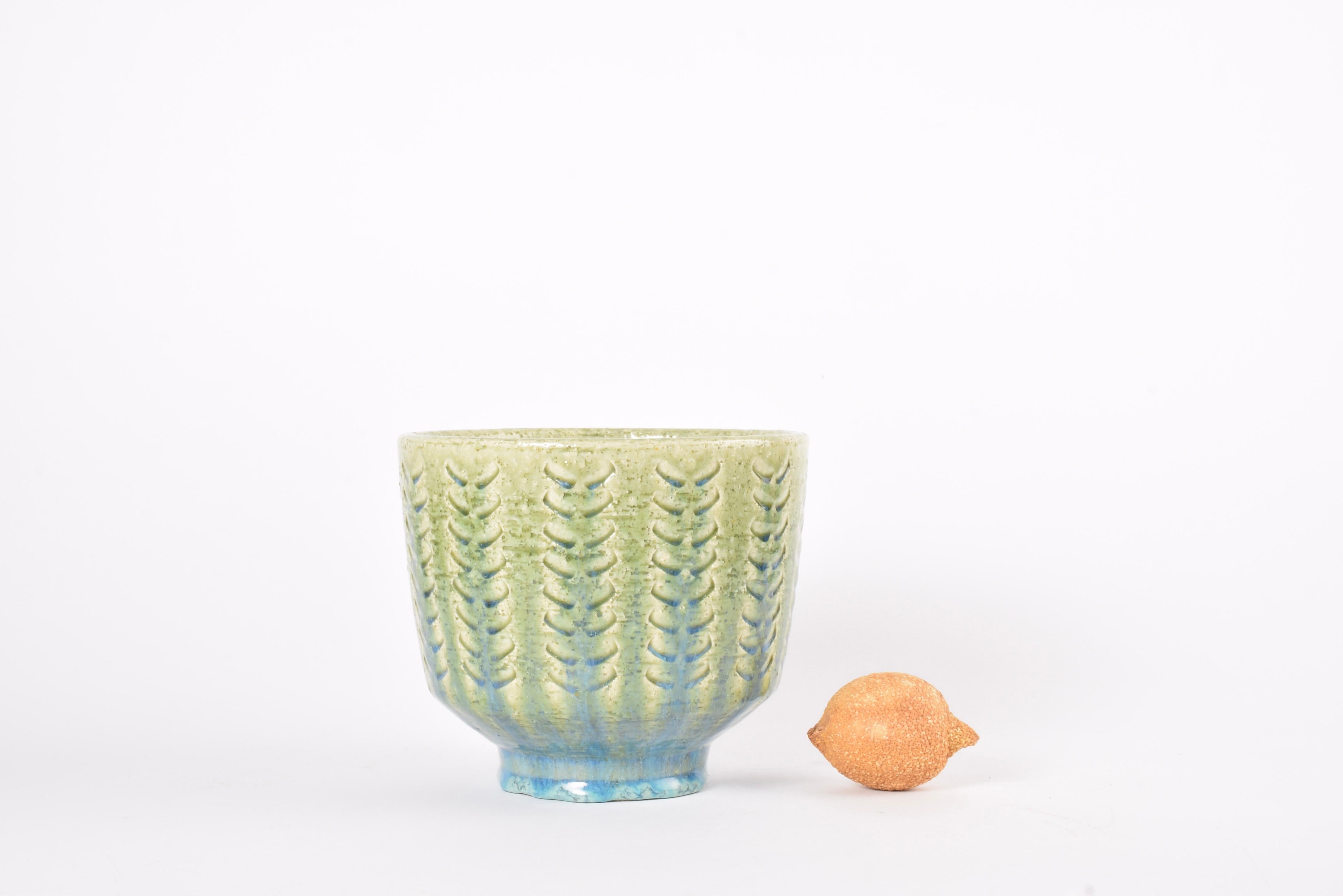 Large ceramic flowerpot by Per Linnemann-Schmidt for Palshus Denmark. Made ca. 1960s.

It is made with chamotte clay which gives a rough and vivid surface. It has a grass green glaze mixed with pale blue glaze over a repeated textured decor.

Fully