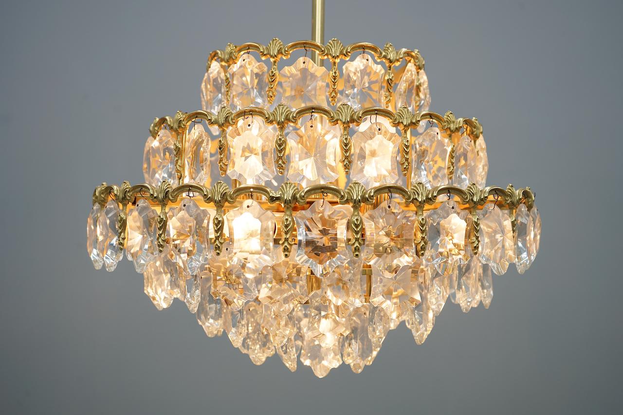 This stunning Crystal glass Chandelier by Palwa from the 1960s is sure to add a touch of elegance and sophistication to any space. With four tiers of sparkling crystals and a brass frame, it is a true statement piece. The chandelier requires 7 E