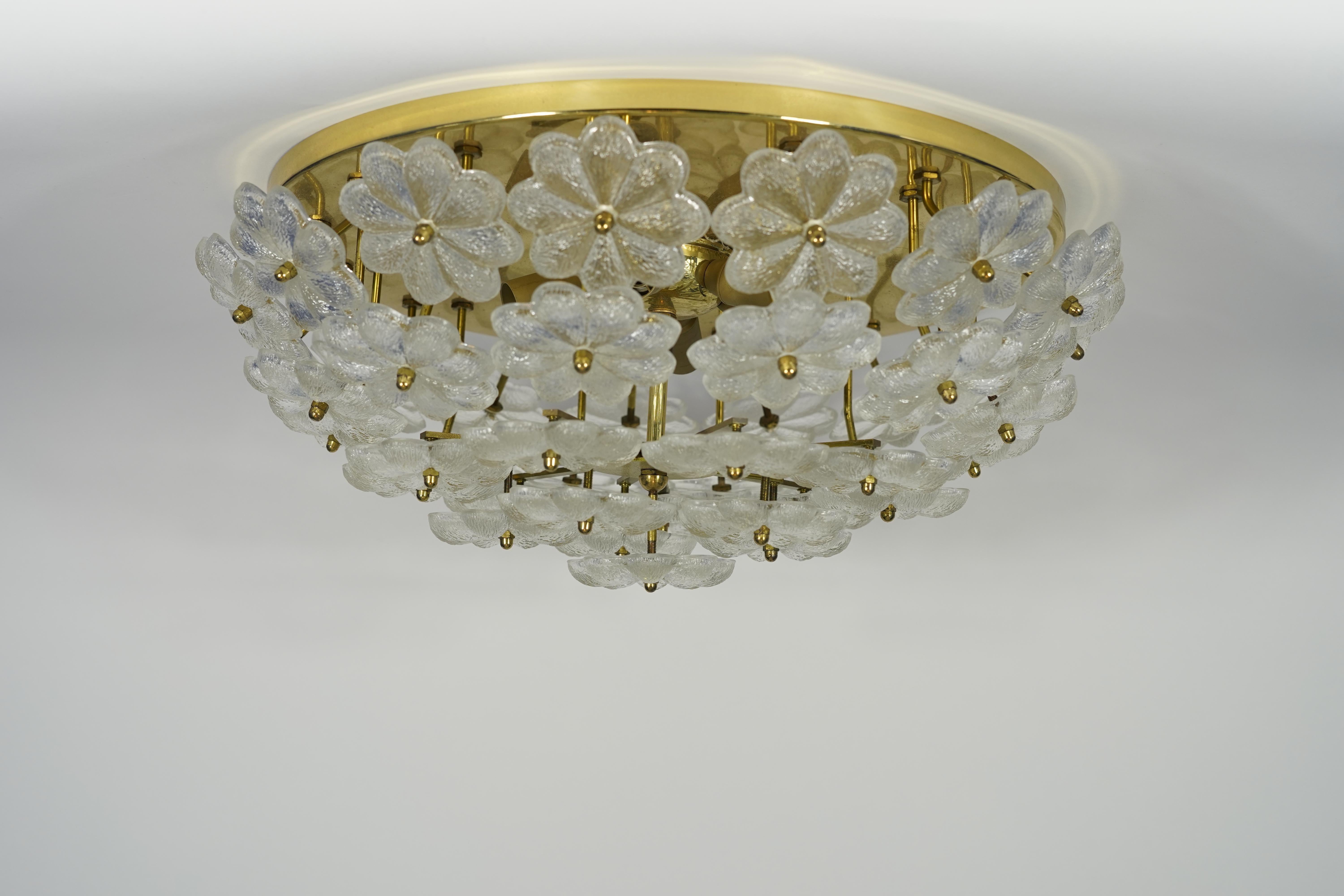 Polished brass base with 6 candelabra sockets, numerous individual large clear glass in the shape of a flower forms a shade.