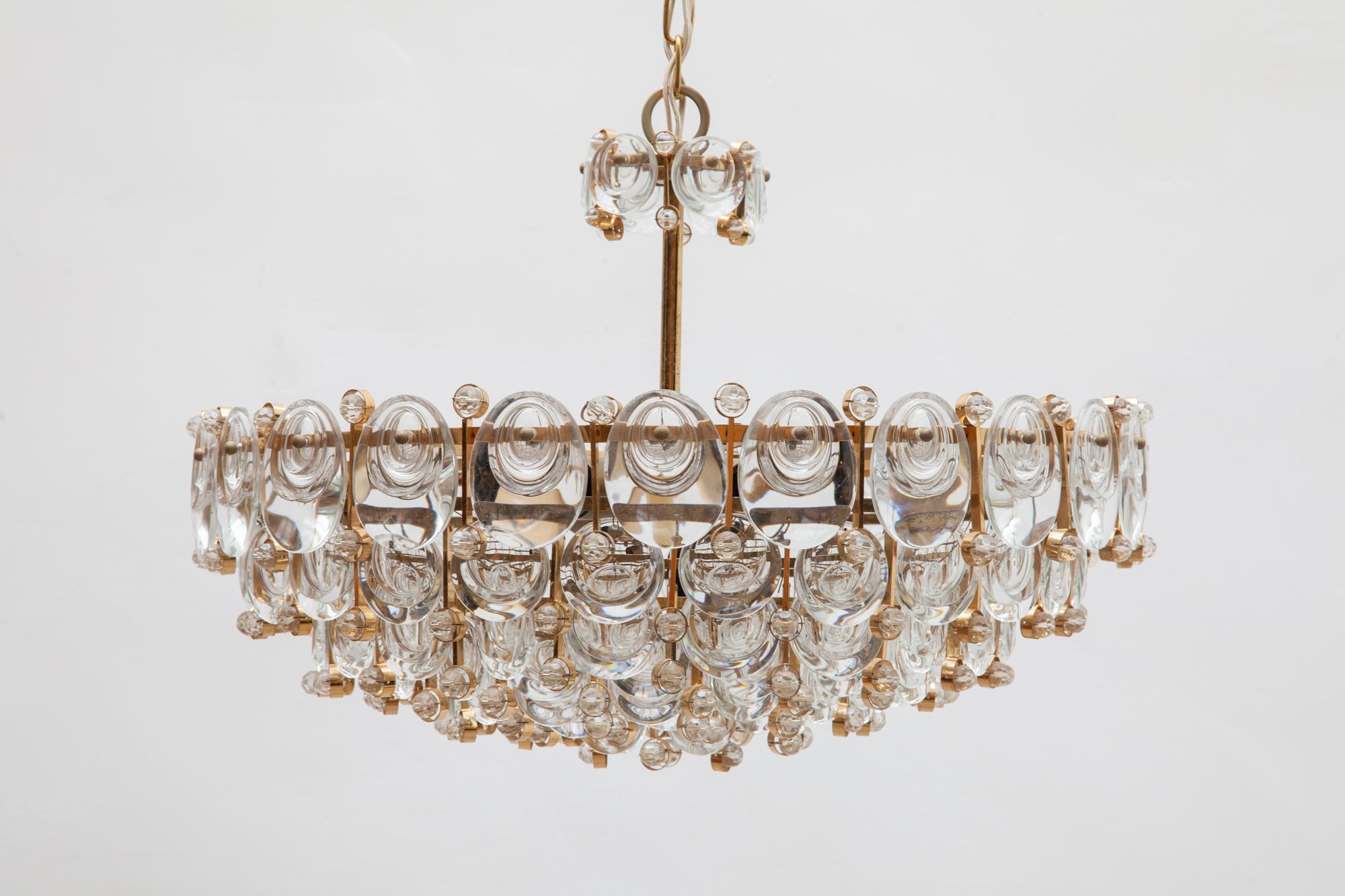 Palwa chandelier seven-tier design with eight lights a gilded brass. A circular structure comprised of small and large rings with dangling optical glass lens crystals inside. Created in Germany in the 1960s. With matching brass chain and flat simple