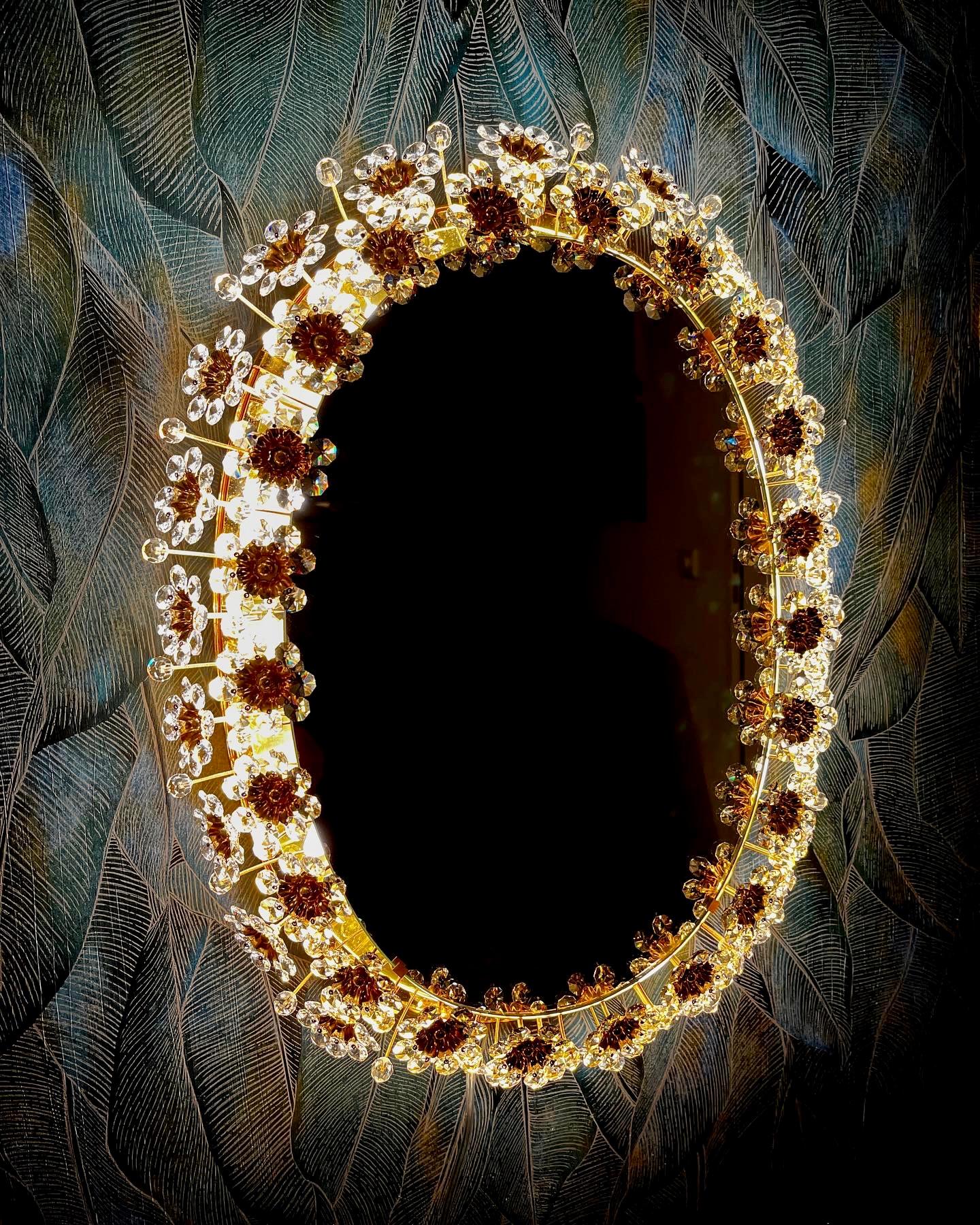 An oval wall mirror by Palme & Walter with indirect lighting and crystal flowers from the 1960s.
Absolutely high-quality workmanship! The brass frame is gold-plated and the flowers are made of crystal. All crystals are present!

This vintage item is
