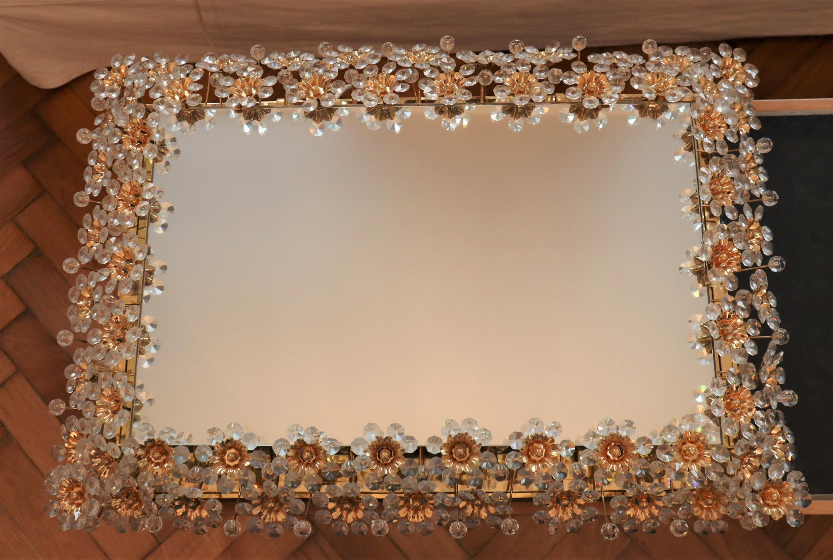 Mid-20th century illuminated rectangular wall mirror by German manufacturer Palwa.
The mirror is framed with a double border of delicate flowers and petals made from faceted crystals and beads that sparkle in the light. 
The frame is made from
