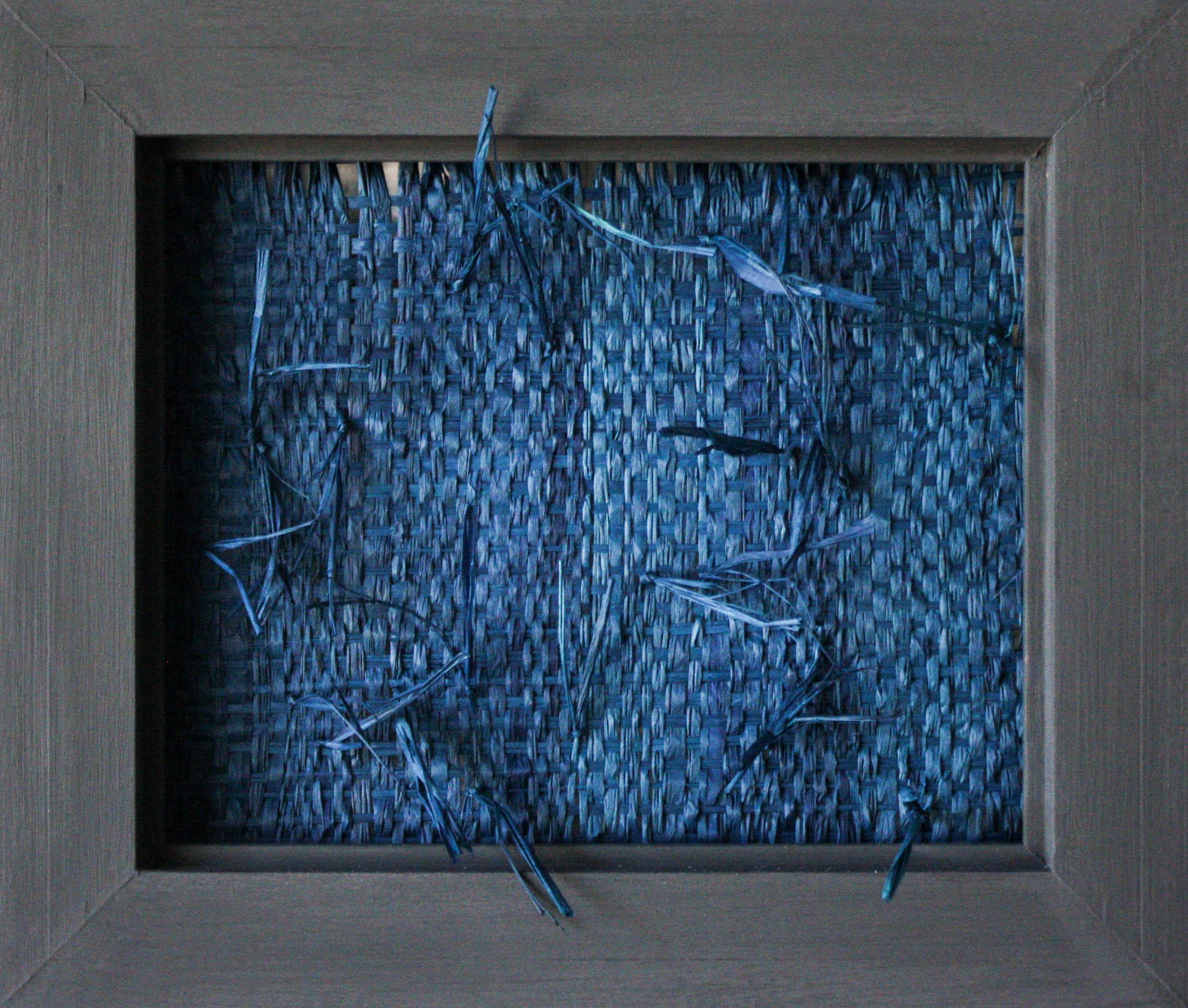 This woven sculptural wall hanging is created using blue raffia mounted inside a wooden frame. Its organic nature is complemented by a few loose pieces that break out of the rectangular scope of the frame. 