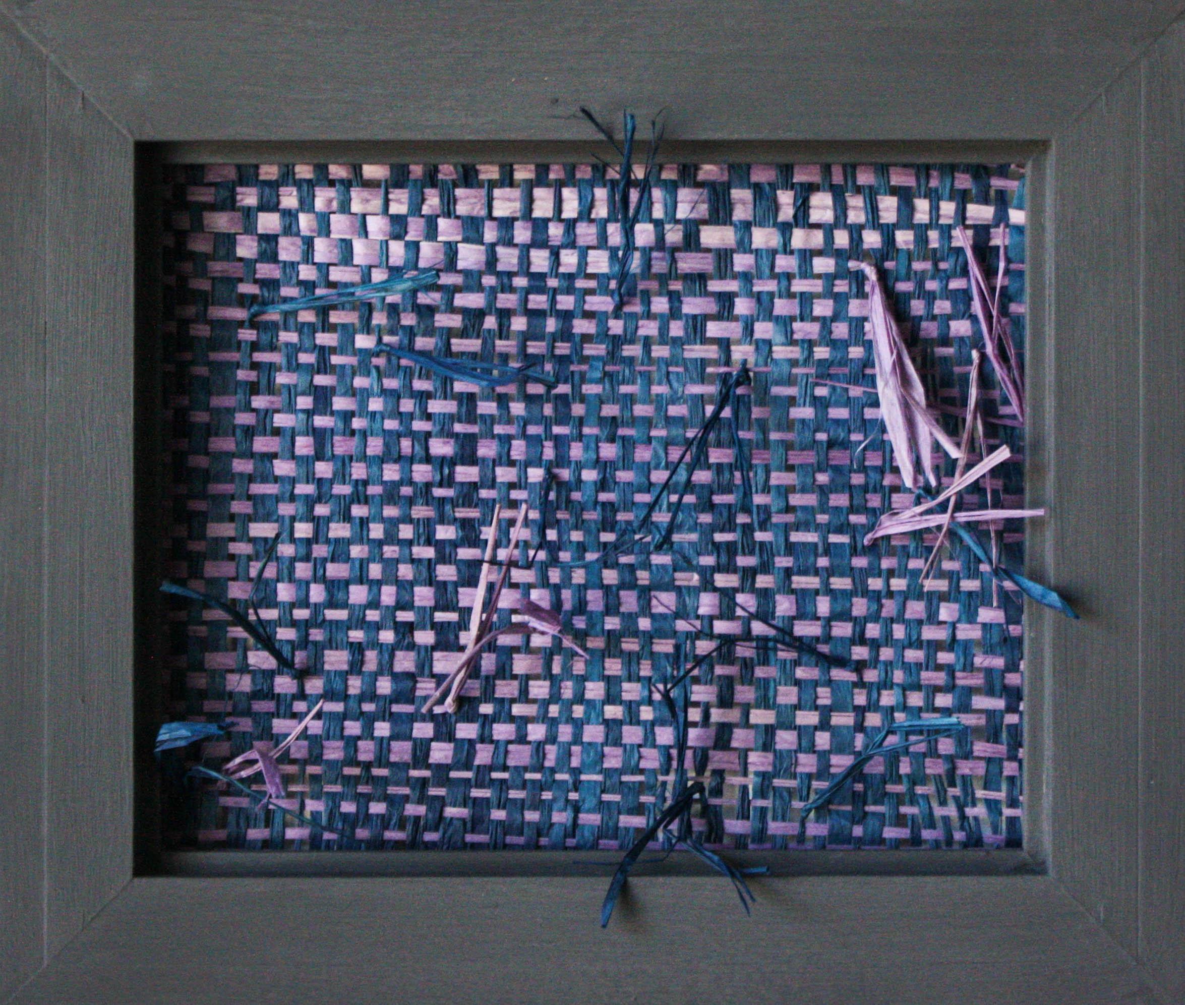 This woven sculptural wall hanging is created using blue and purple/violet raffia mounted inside a wooden frame. Its organic nature is complemented by a few loose pieces that break out of the rectangular scope of the frame.