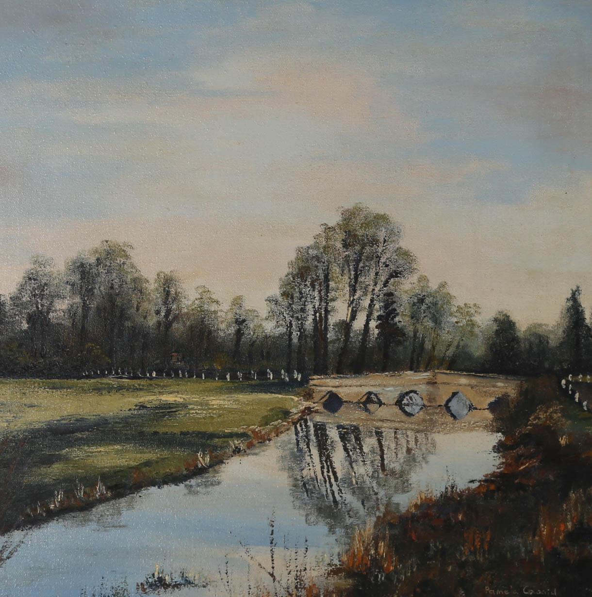 A delightful depiction of a river landscape, painted by British artist Pamela Coward. In the foreground reeds and grasses line the river bank in expressive autumn colours. A beautiful village bridge leads on to woodland trees that shimmer in the