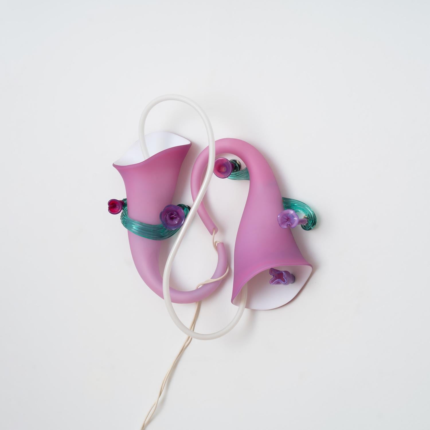 With a delicate yet playful form, Pamela Sabroso's 'Luminous Wallflowers I' sconce invites the viewer to bask in the soft neon glow. The muted, matte pink finish of the mouth-blown glass is accented with waves of glossy teal and violet stems and