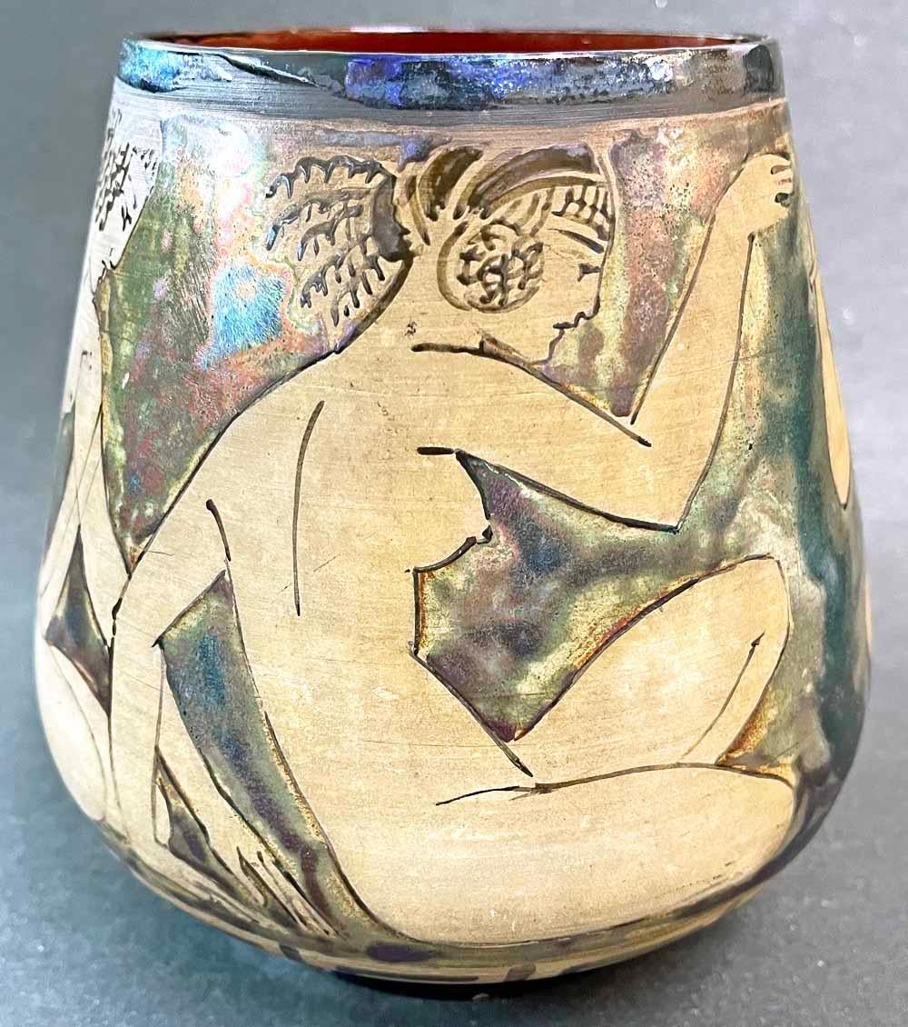 Striking and sensuous, this 1920s French vase depicts a flute-playing nude Pan figure flanked by three nude female figures with Greek attributes, all set in a lustrous blue surround finished in iridescent glazes.  The entire scene seems like a