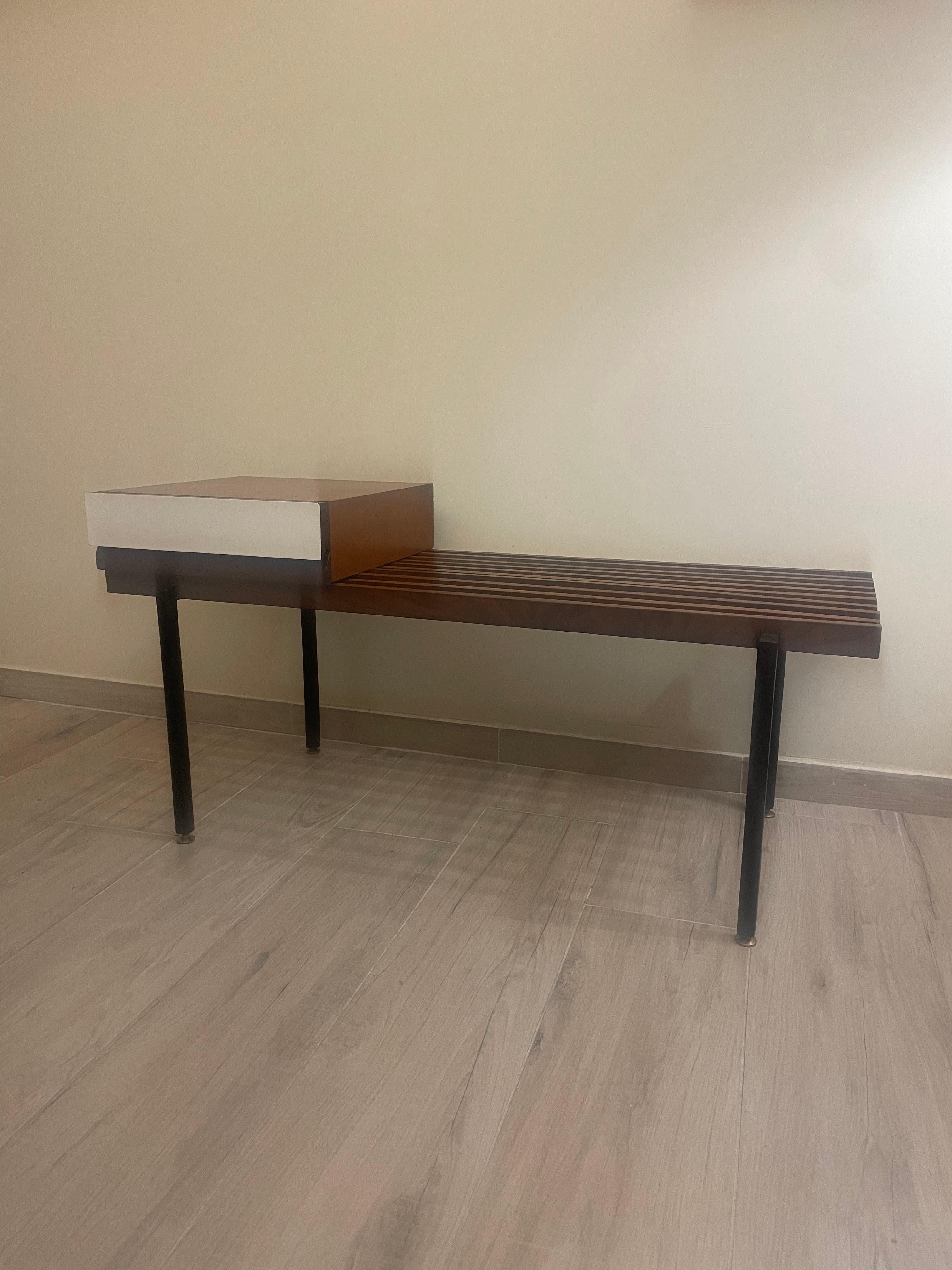 1960s bench made of teak wood and square, black enameled metal frame with brass ferrules.

The seat composed of the classic set of teak wood rods is accompanied by a pull-out storage compartment with a white Formica front panel.
Useful for being