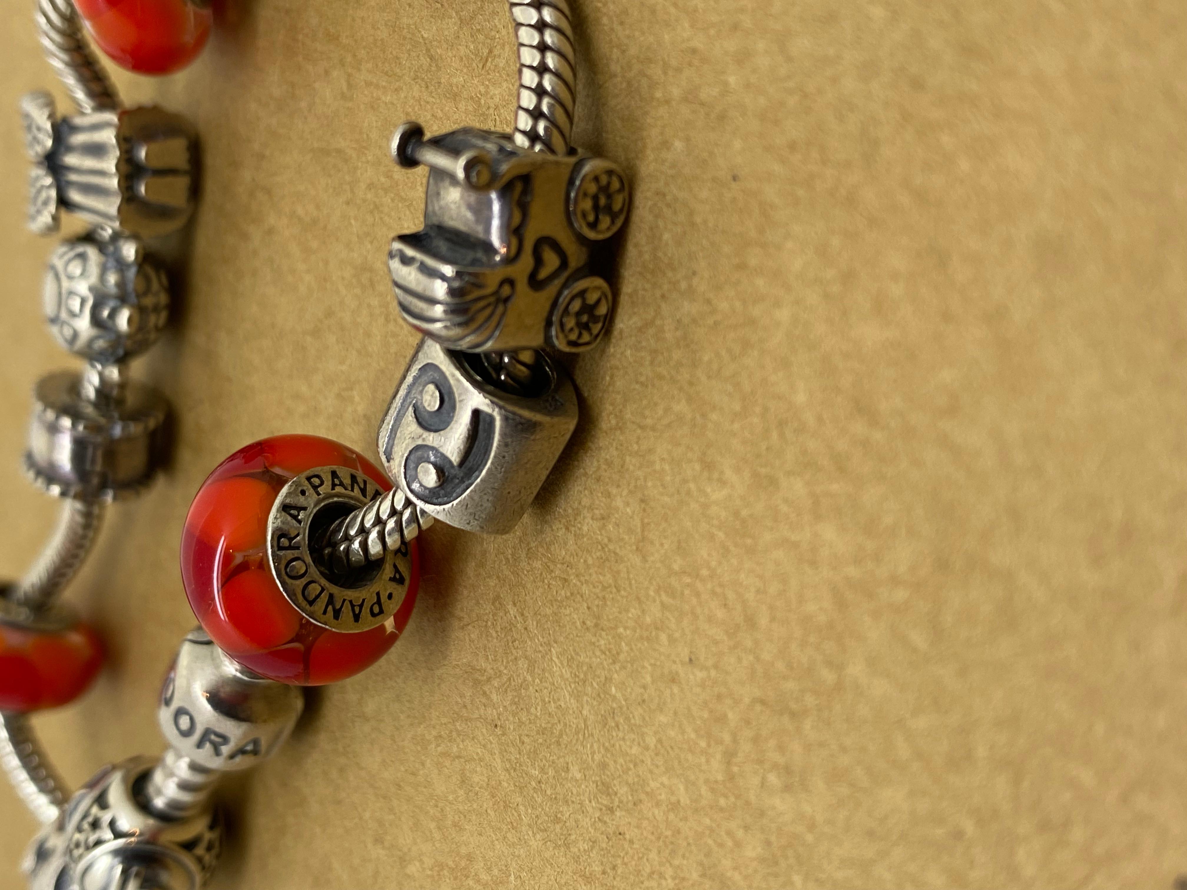 This 925 Sterling Silver Charm Bracelet by Pandora 
is comprising 11 charms,
performed in Sterling Silver,
including 3 red Murano glass charms, 
zodiac charms: Libra & Cancer charms, 
cherub charm, pram & turtle charms, 
letter M charm, decorated