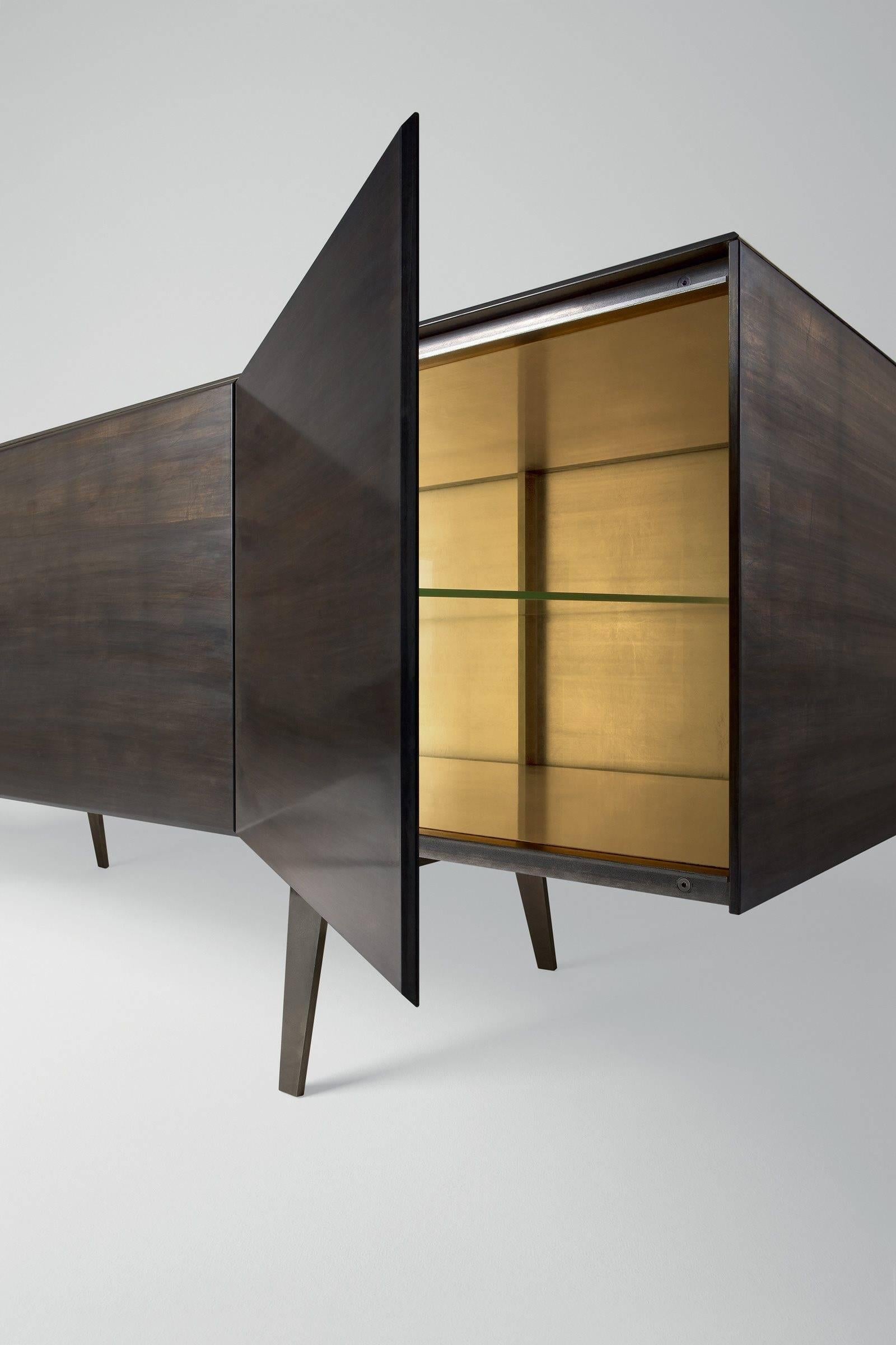 Sideboard in 8 mm tempered glass covered by gold leaf applied by hand with an exclusive system. 
Thanks to this process the unit has an irregular and unique finish outside and a gold finish inside. 
Metal structure lacquered bronze color with