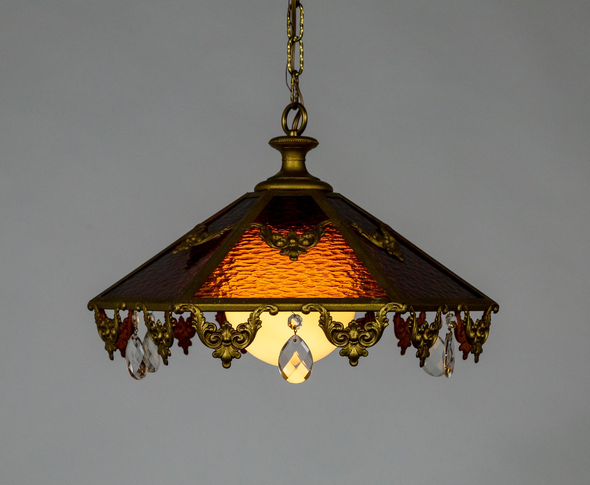 An antique pendant light with 6 rippled, stained glass panes forming a coolie shape; alternating between amber and red-brown. With a large, white, globe shade and gold painted trim and garland details with large, cut crystal drops hanging from each