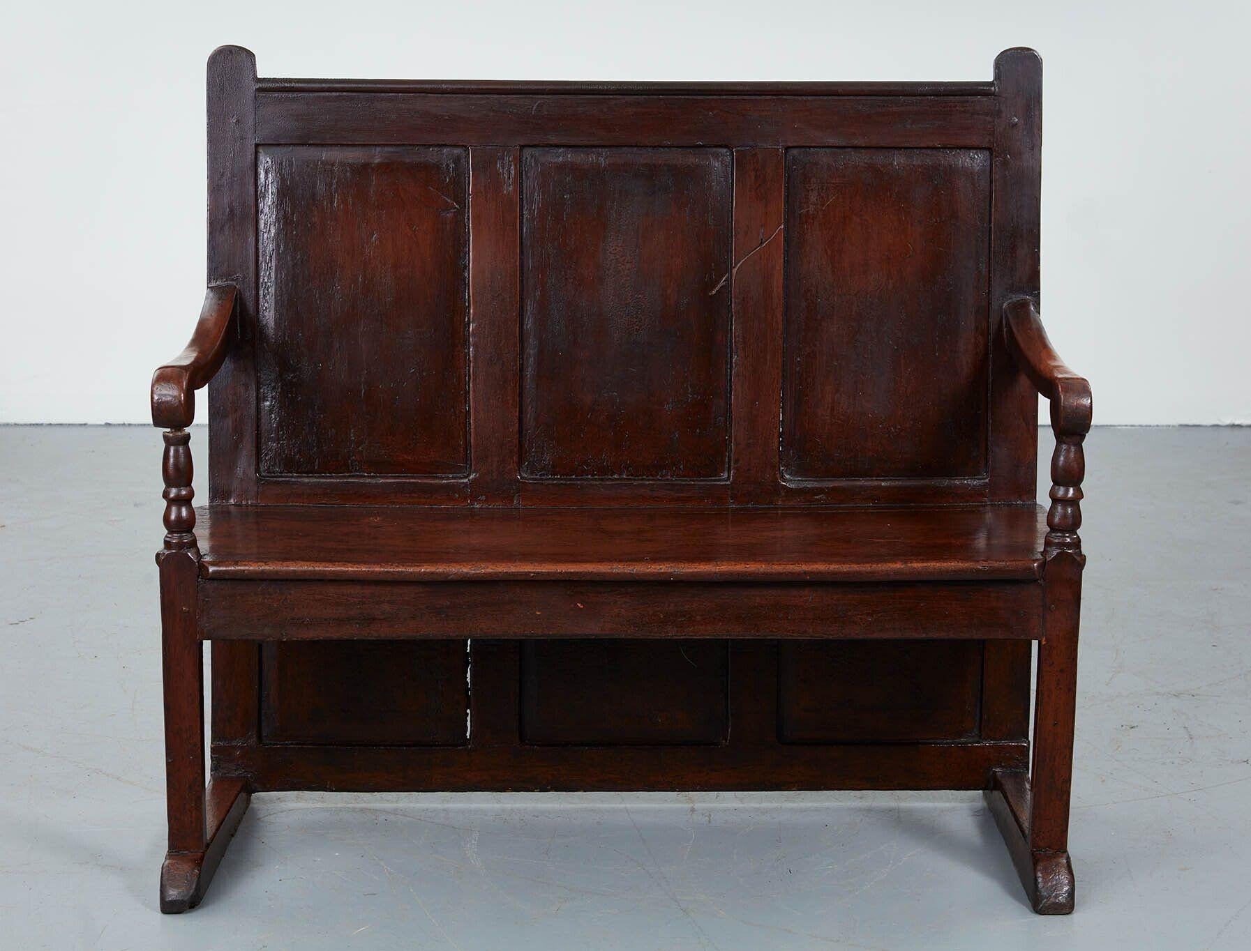 An 18th century West Country painted pine settle, the raised panel back extending almost to the floor (to keep out drafts), on open sled-form feet, with shaped arms, and raised ears to the paneled back, retaining wonderful old scumbled paint surface.