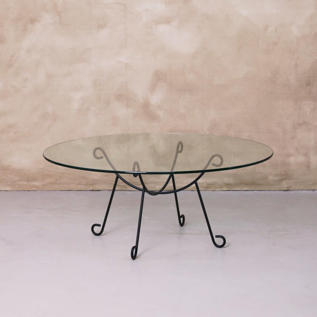 Preciosa mesa de centro de hierro y cristal inspirada en el diseño francés. Base curvada y arqueada, con recubrimiento de polvo en acabado negro mate y tapa redonda de cristal. Múltiples disponibles, se venden individualmente. Hecho en Los Ángeles.