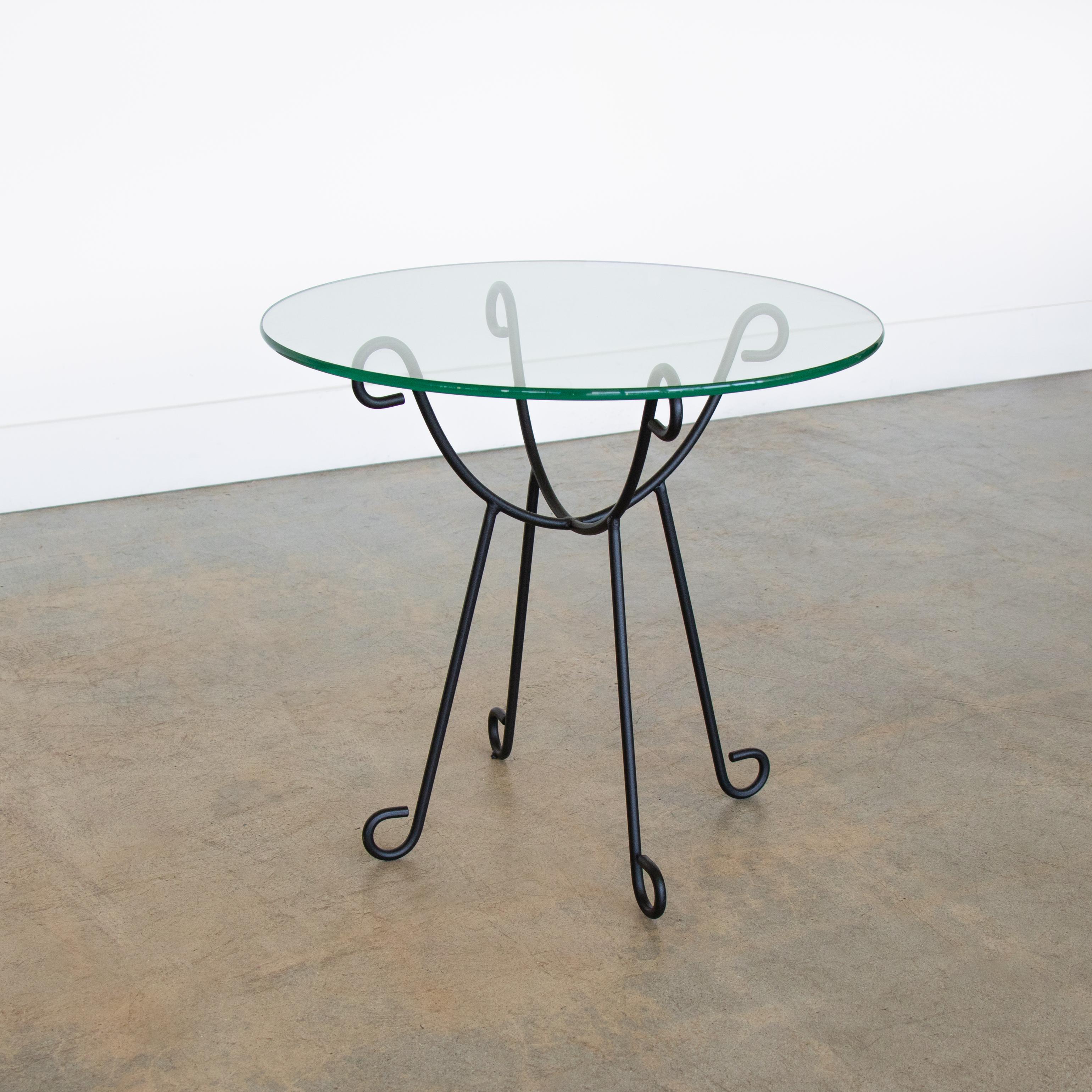 Magnifique table d'appoint en fer et en verre inspirée du design français. Base courbée et arquée, revêtue de poudre dans une finition noire mate avec un plateau rond en verre. Disponible en plusieurs exemplaires, vendus individuellement. Fabriquée