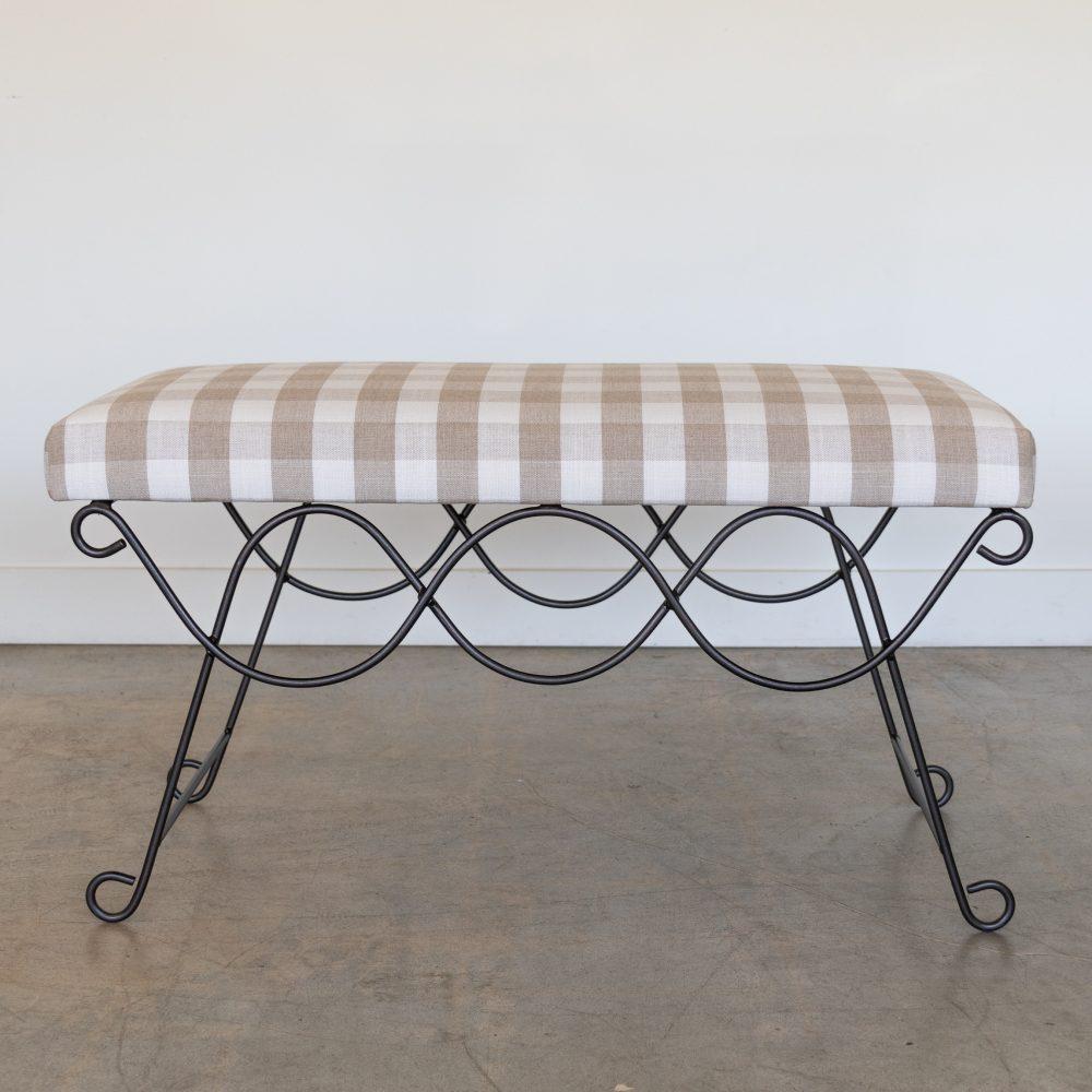 Beautiful iron bench with curved and looped base painted in a matte black finish inspired by French design. Rectangular cushioned seat upholstered in a tan gingham linen fabric or can be COM. Multiple available, sold individually. Made in Los