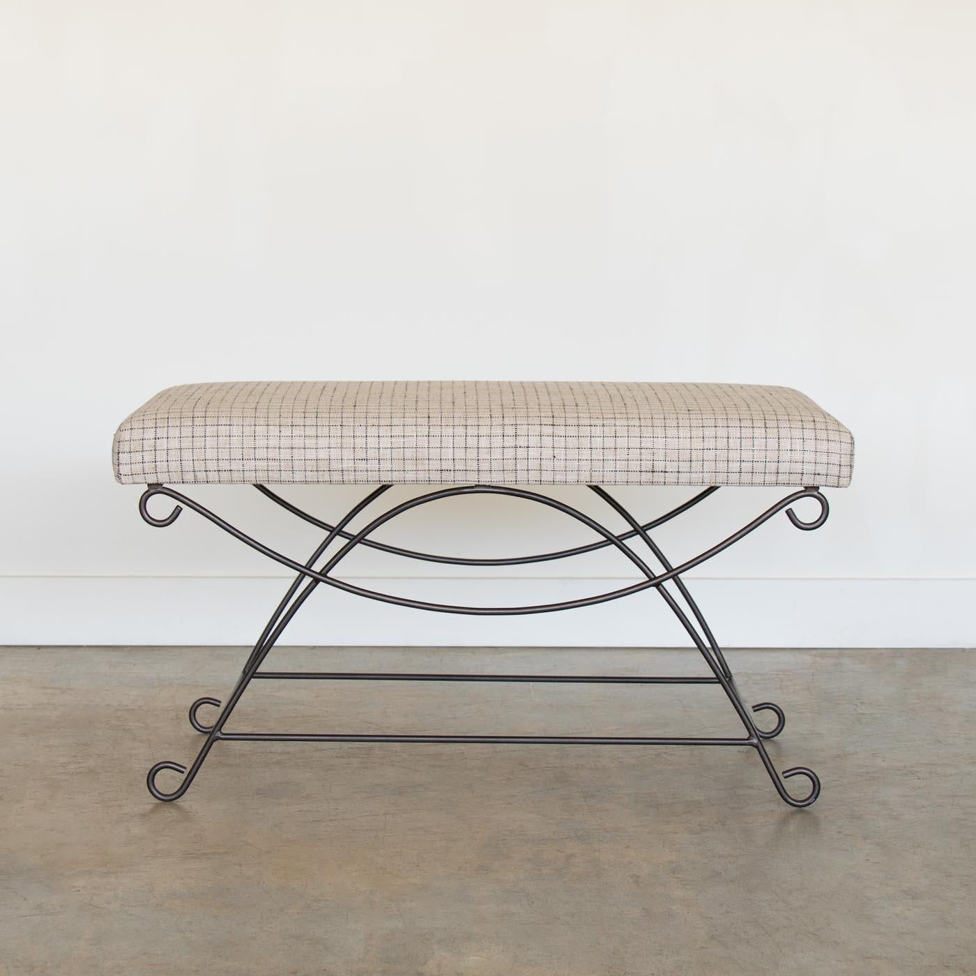 Beautiful iron bench with curved and looped base painted in a matte black finish inspired by French design. Rectangular cushioned seat upholstered in a linen check fabric or can be COM. Multiple available, sold individually. Made in Los Angeles.