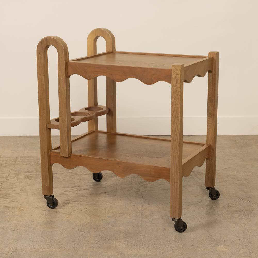 Beautiful walnut wood bar cart newly made in Los Angeles. Rectangular cart with two tiers and carved wavy scalloped detail on shelf edges. Curved wood handles and 3 bottle compartments on lower shelf with new rolling casters. Beautiful and
