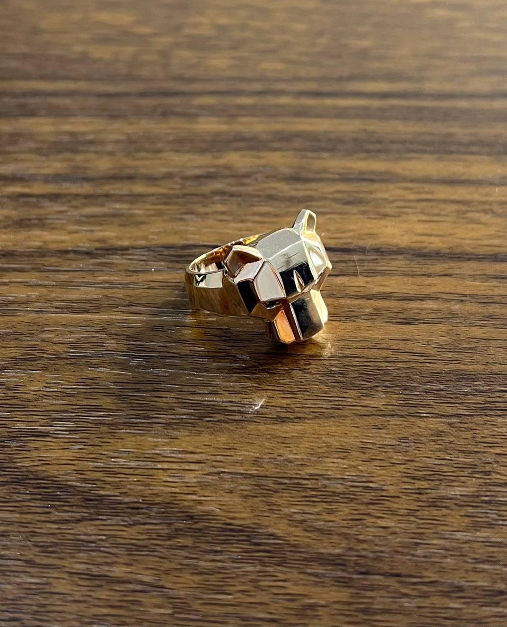 This captivating piece features a bold design in lustrous gold. The ring showcases a sculpted panther head with sharp, geometric lines. The eyes are set with vibrant green emeralds, adding a touch of vivid color and intensity.
The band is thick and