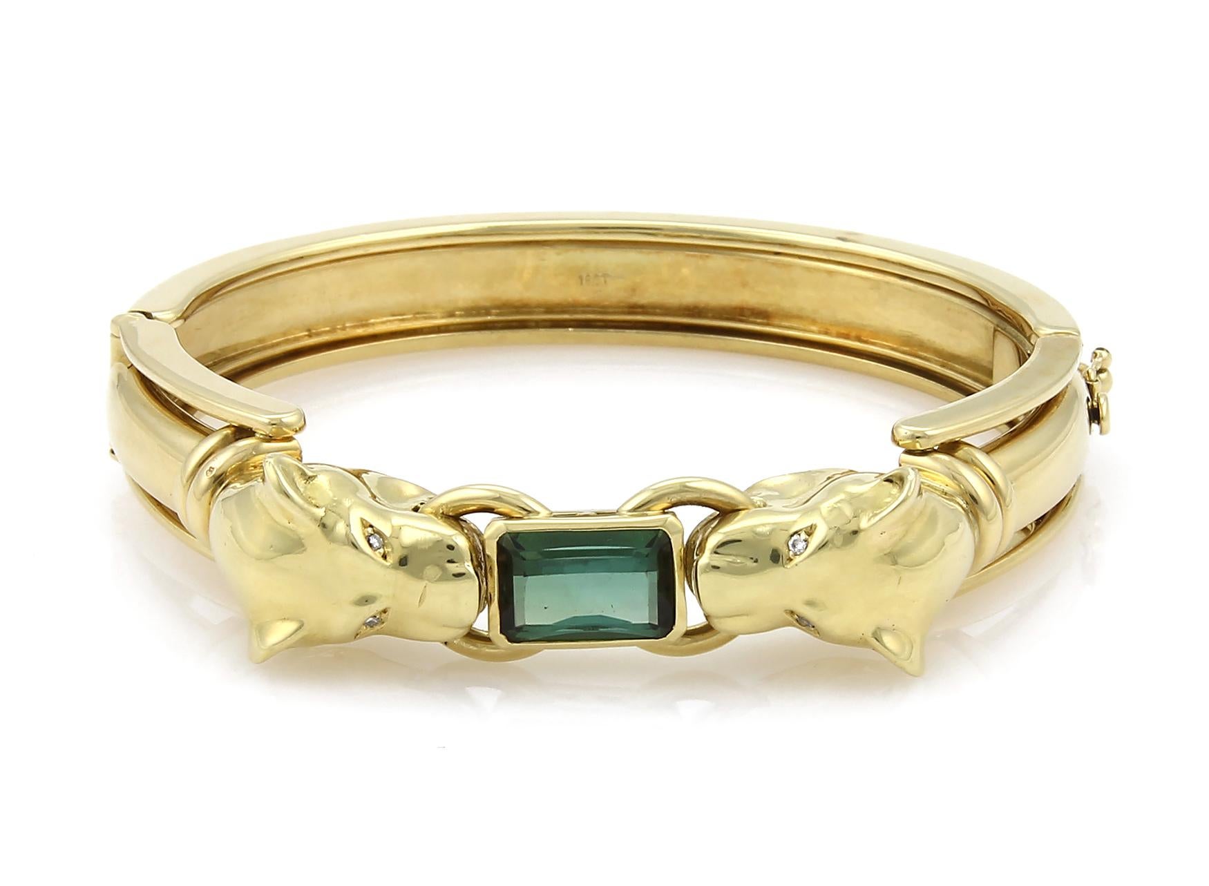 This is an amazing sculpted bracelet, forged from 18k yellow gold with a high polished finish it features a double panther head with a stunning emerald cut green tourmaline gemstone set between the panthers mouth, their eyes are small round diamonds