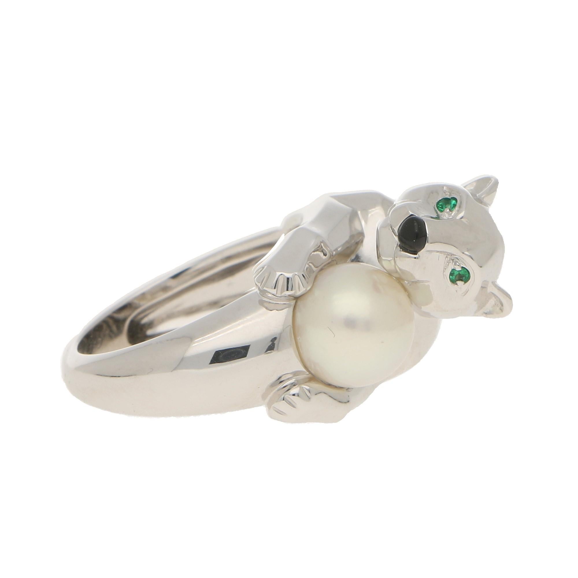 A classic Cartier Panthère ring set in solid 18 carat white gold. The ring prominently features a polished panther shaped motif which holds a beautiful white cultured pearl. The panther is set with vibrant emerald green eyes and a little button onyx