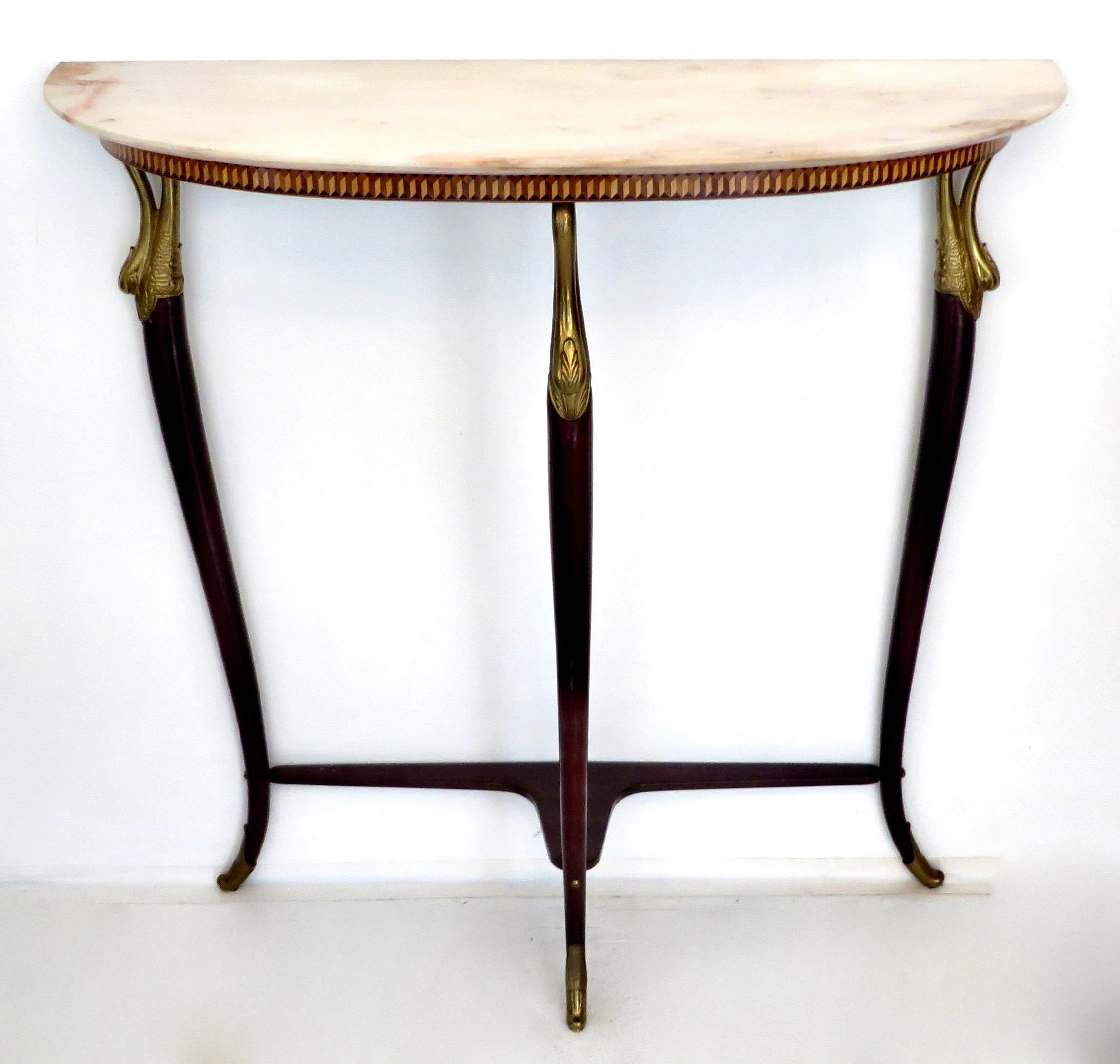 Italian neoclassical Art Deco demilune console attributed to Paolo Buffa with a cream peach Brescia Primavera marble top. The apron has a finely done inlay. 
There are carved gilded swan supports at the top of the hand-carved mahogany legs
