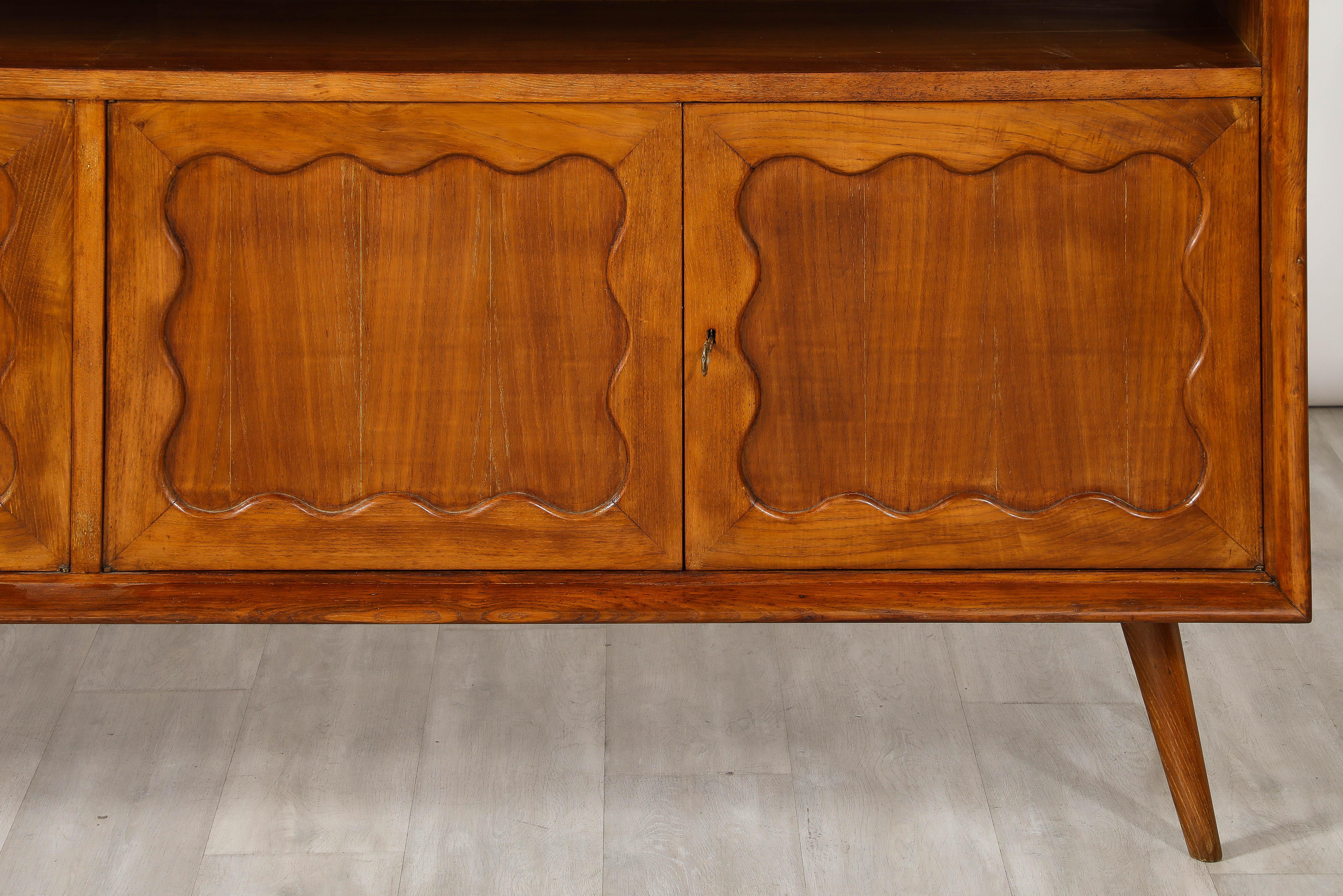 A charming hand-carved walnut and oak credenza or sideboard by Italian designer Paolo Buffa, circa 1950.   The four doors with scalloped carving open to reveal internal shelves, with three enclosed small drawers with brass ring pulls on the right
