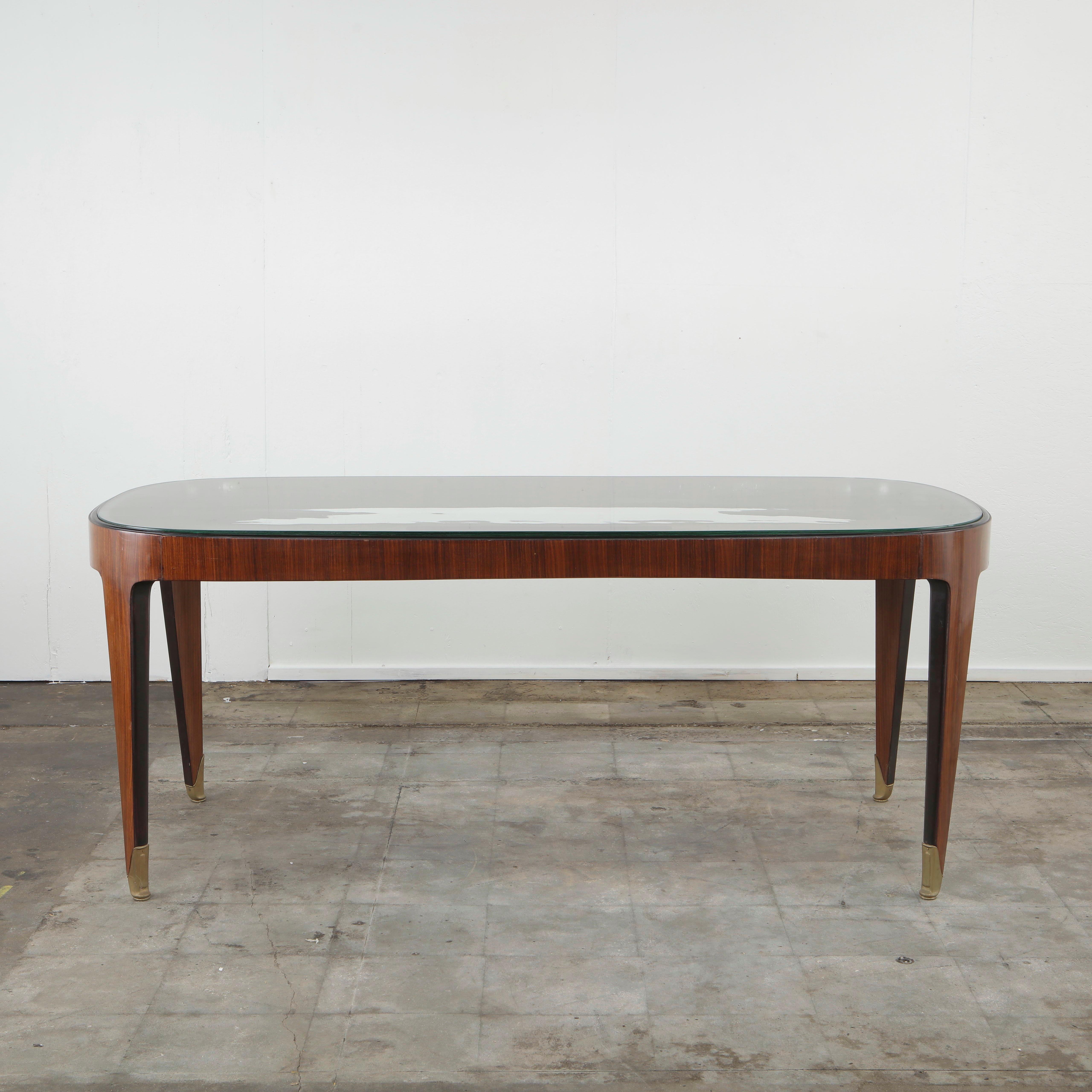 Elegant dining table from Italy, 1940s, featuring a gently curved rectangular form with exceptional craftsmanship typical of the mid-century era. The structure is made of richly grained rosewood with beautifully tapered legs ending in solid brass