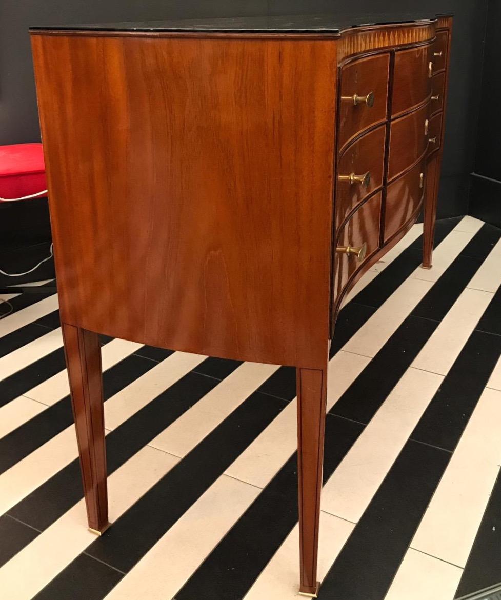 An exquisite nine-drawer wooden commode with inlaid decoration, beautiful brass handles and brass sabots designed by the Italian architect and designer Paolo Buffa. It has a beautiful wavy shape at the front and glass on top. It has been completely