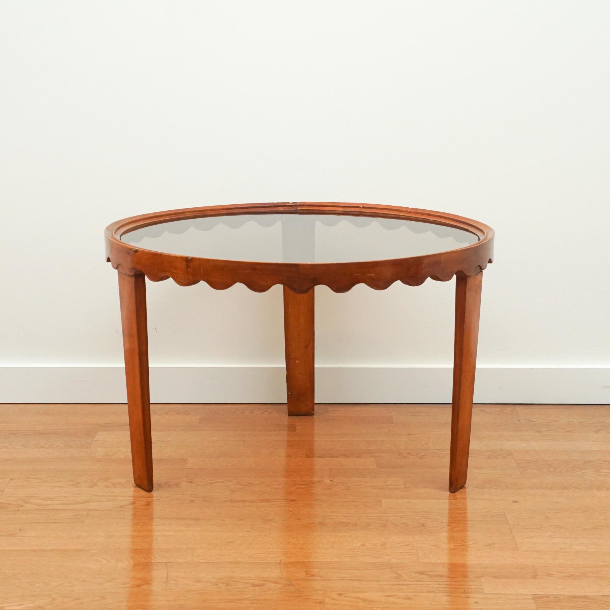 This exquisite accent table was designed by Paola Buffa in the 1940s. Featuring a scalloped apron design, three tapered square-cut legs and a smokey glass top, the table adds a sculptural elegance to any interior. Consider it for traditional spaces