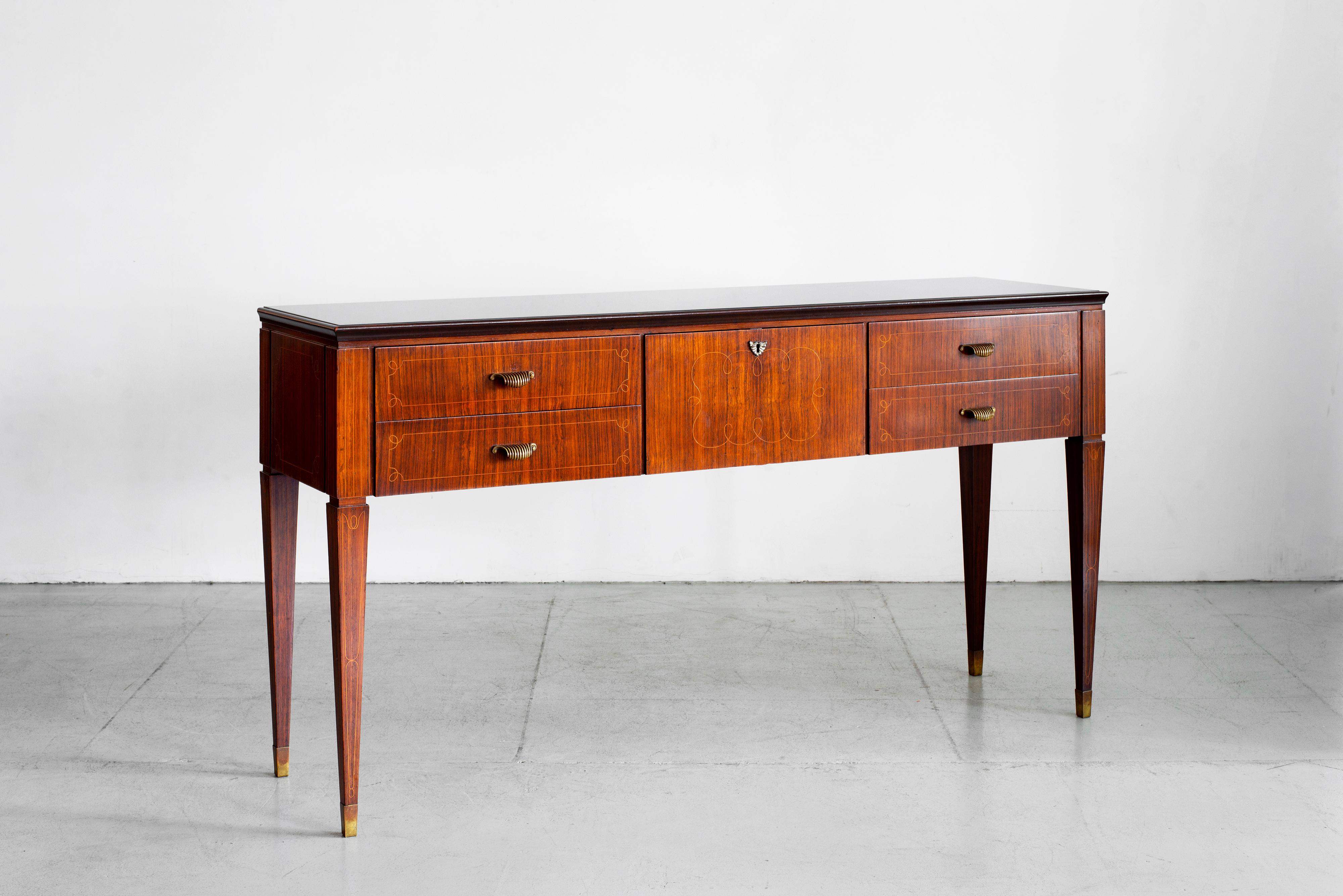 Gorgeous sideboard attributed to Paolo Buffa, circa 1940's
Rosewood with opaque black glass top and tapered legs 
Beautiful brass scalloped handles.
Four drawers with ornate inlay 
1 cabinet door with original key opens for more storage.