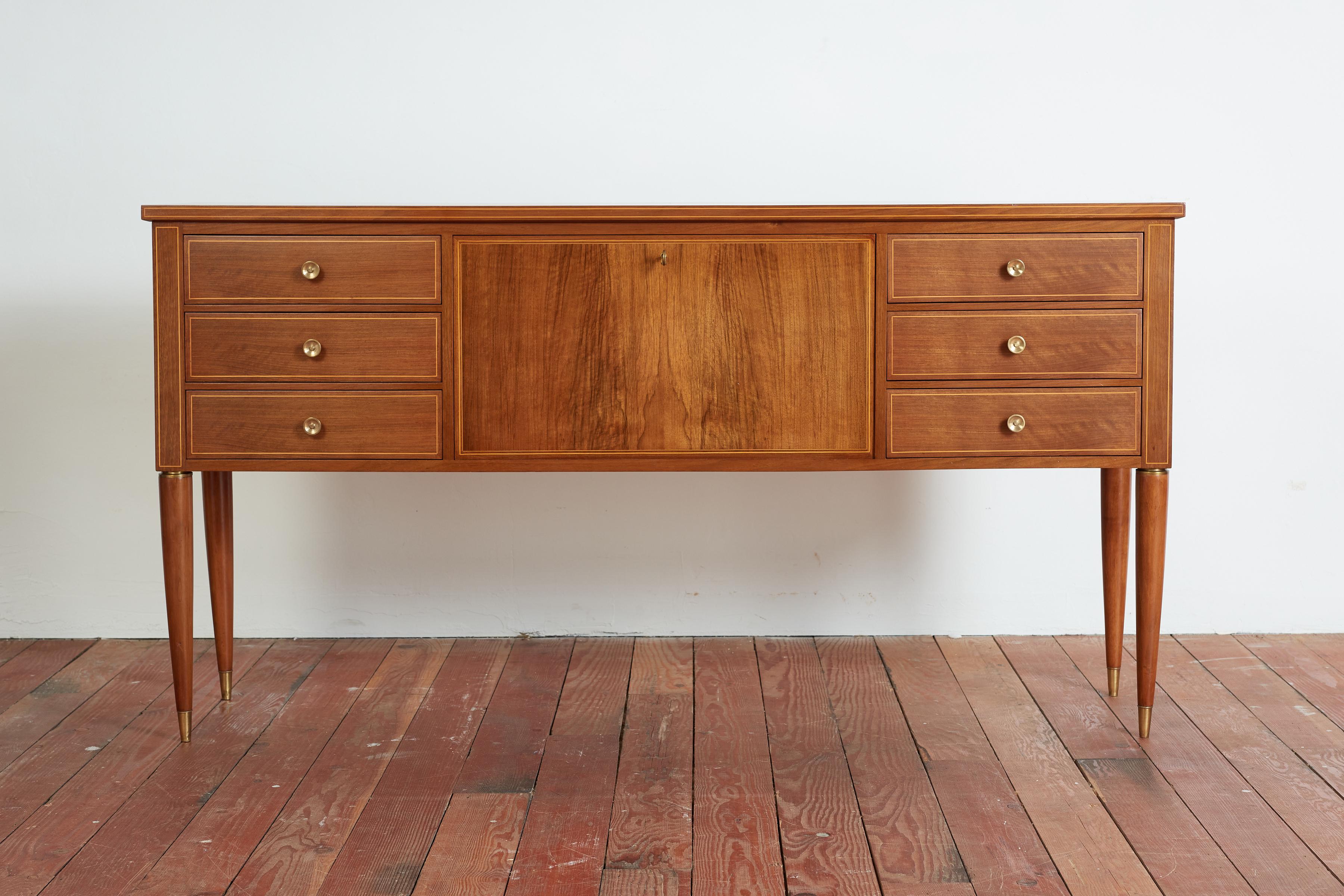 Gorgeous sideboard by Paolo Buffa - Italy, 1940's
Walnut with wood inlay trim throughout with signature tapered legs and brass accents.
Cabinet has 3 drawers on each side of drop down compartment with glass shelf. 


Italy 1940s. 